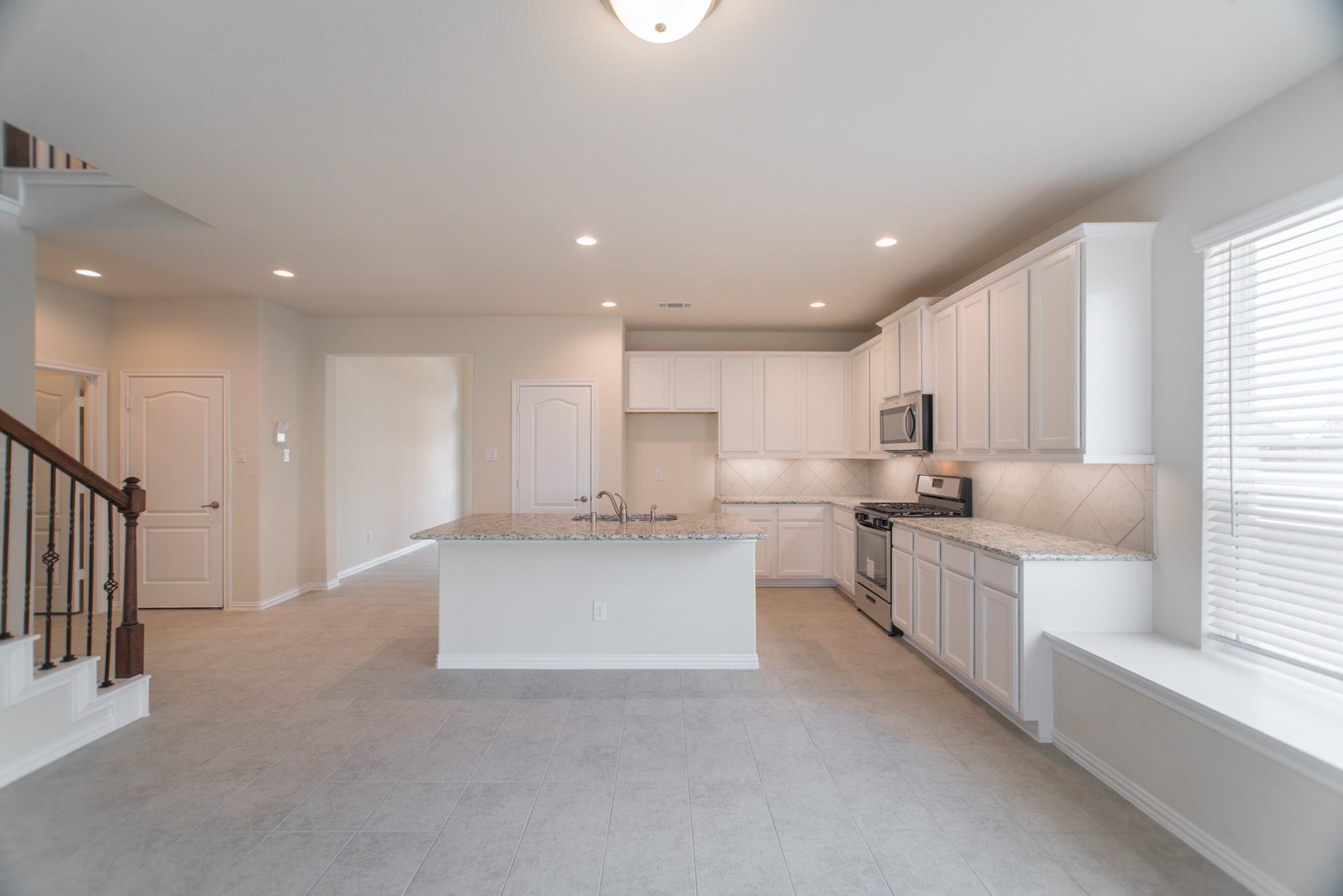 Vacant kitchen with white cabinetry, granite island, stainless steel appliances, and a bright window.