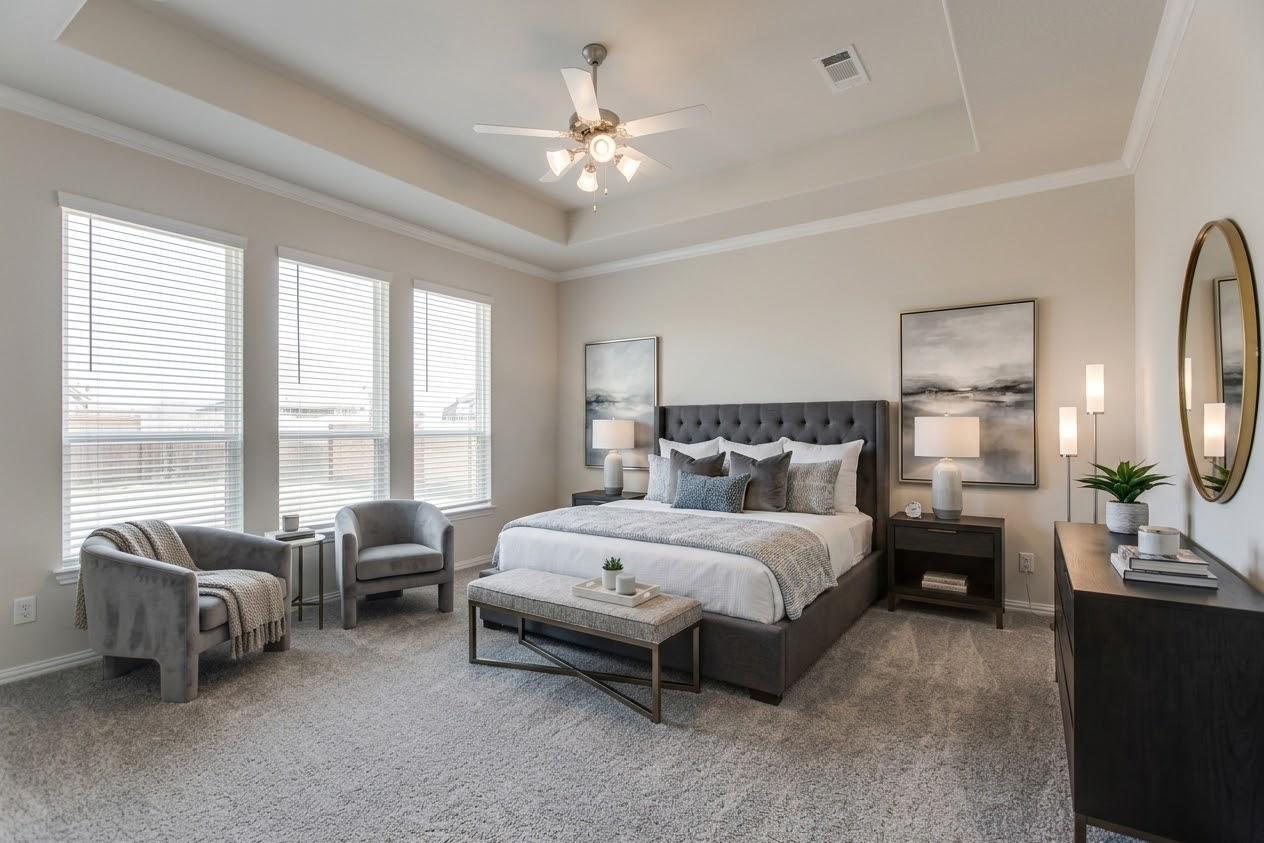 Staged bedroom with a king bed, tray ceiling, ceiling fan, and three tall windows.