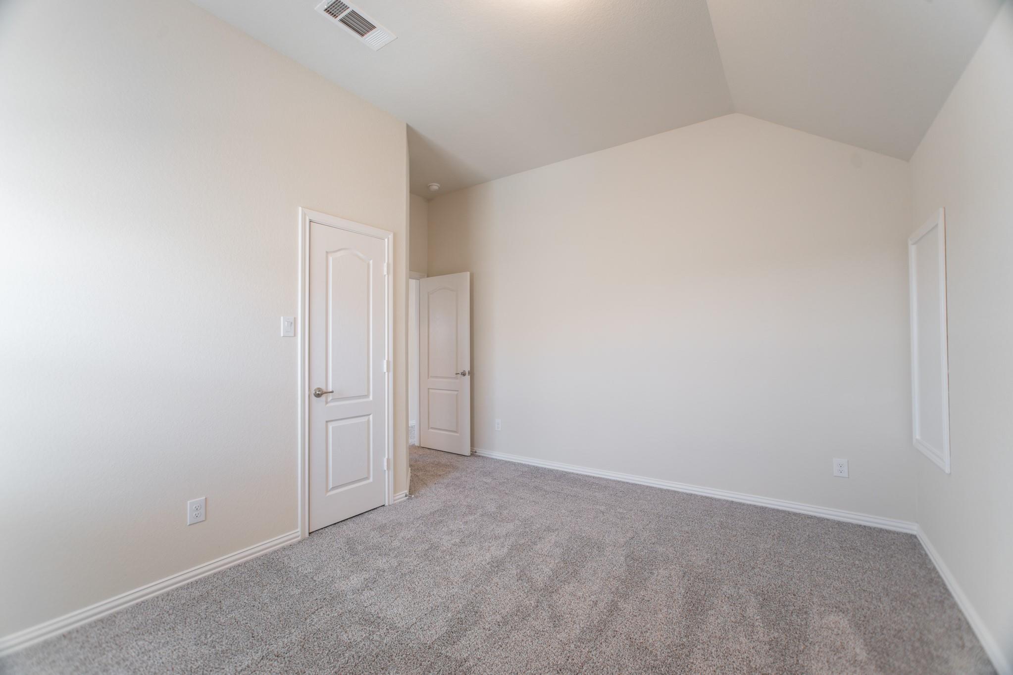 Empty carpeted bedroom with a vaulted ceiling and white paneled doors