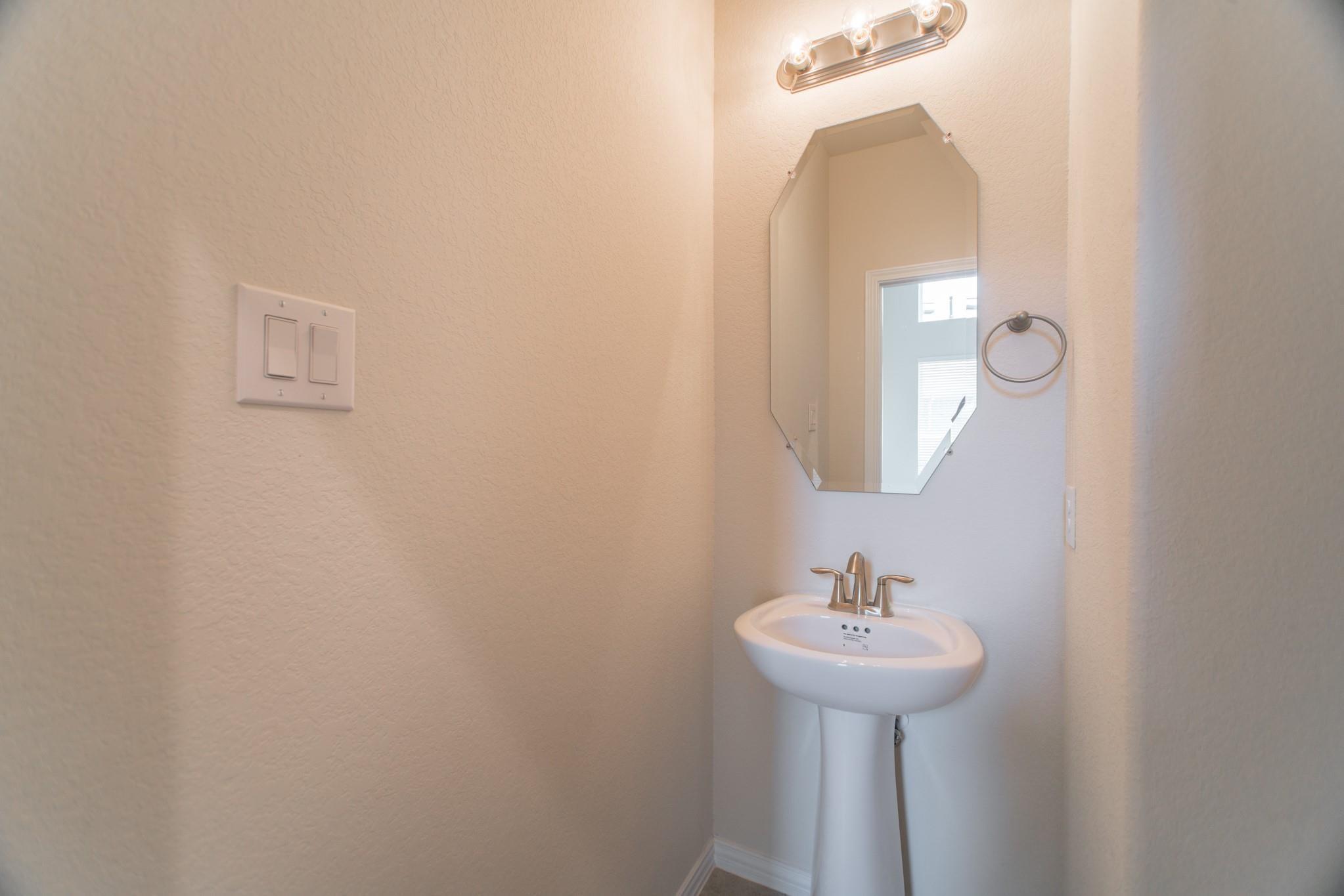 Small bathroom with a white pedestal sink, angular mirror, and chrome fixtures.