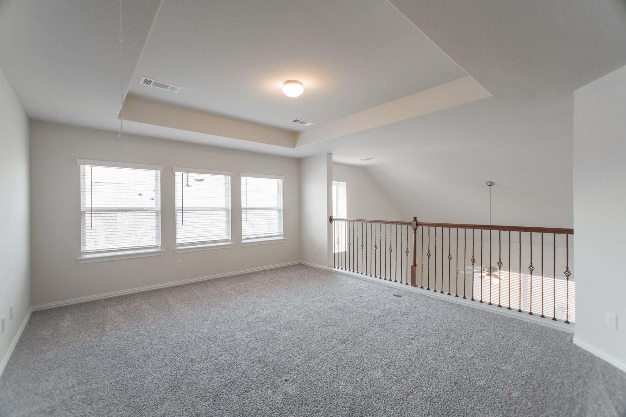 Unfurnished upstairs loft with gray carpet, three windows, a tray ceiling, and a dark metal railing.