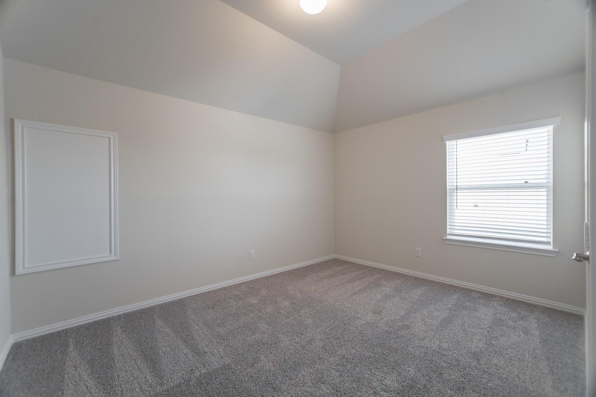Vacant bedroom with gray carpet, vaulted ceiling, and a window with white blinds.