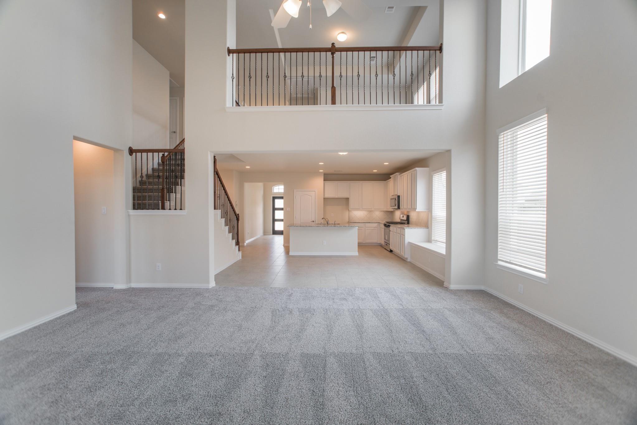 Open-plan living room and kitchen with gray carpet, white cabinetry, and an upstairs landing.