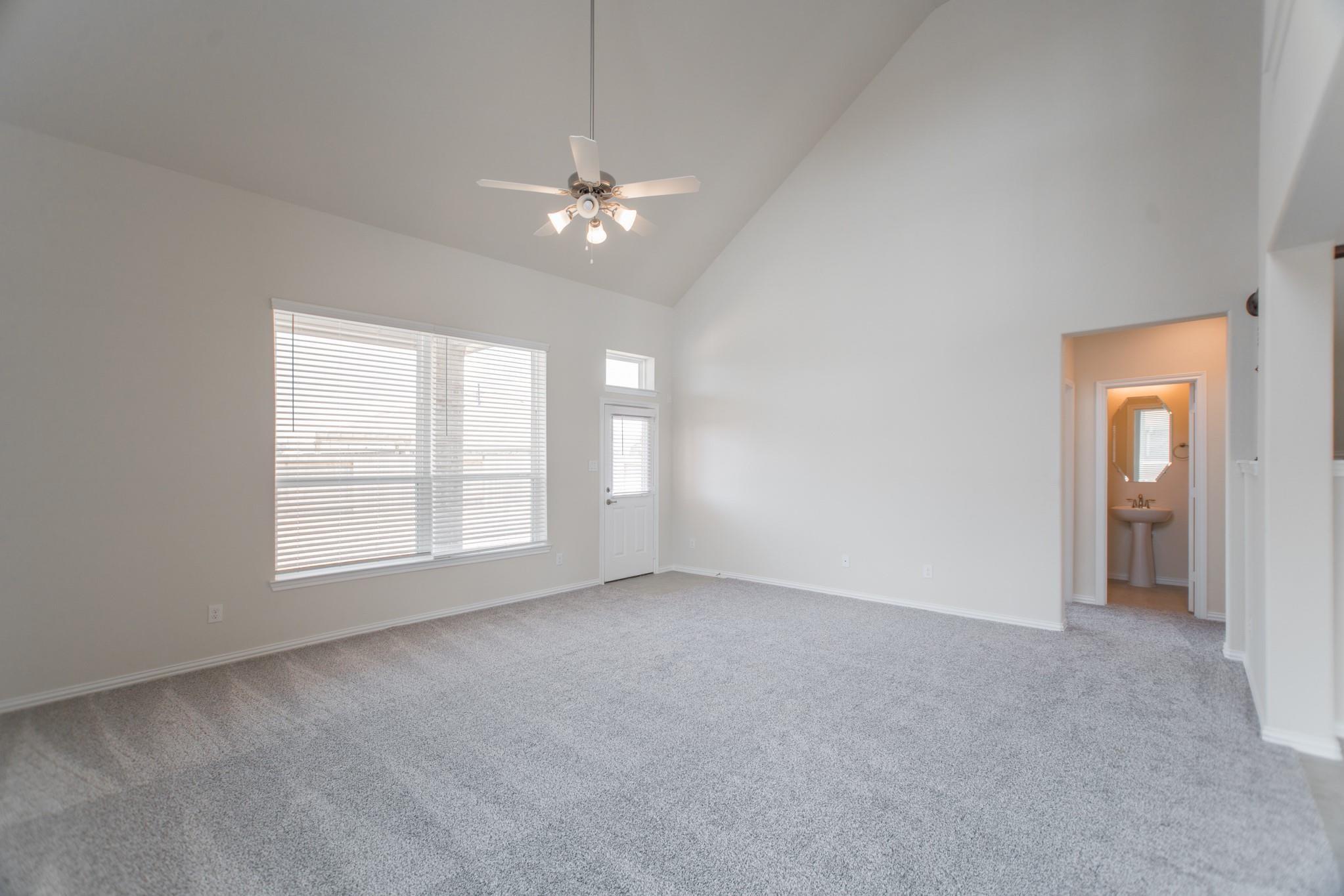 Empty carpeted bedroom with a vaulted ceiling, ceiling fan, and doorway to a bathroom.