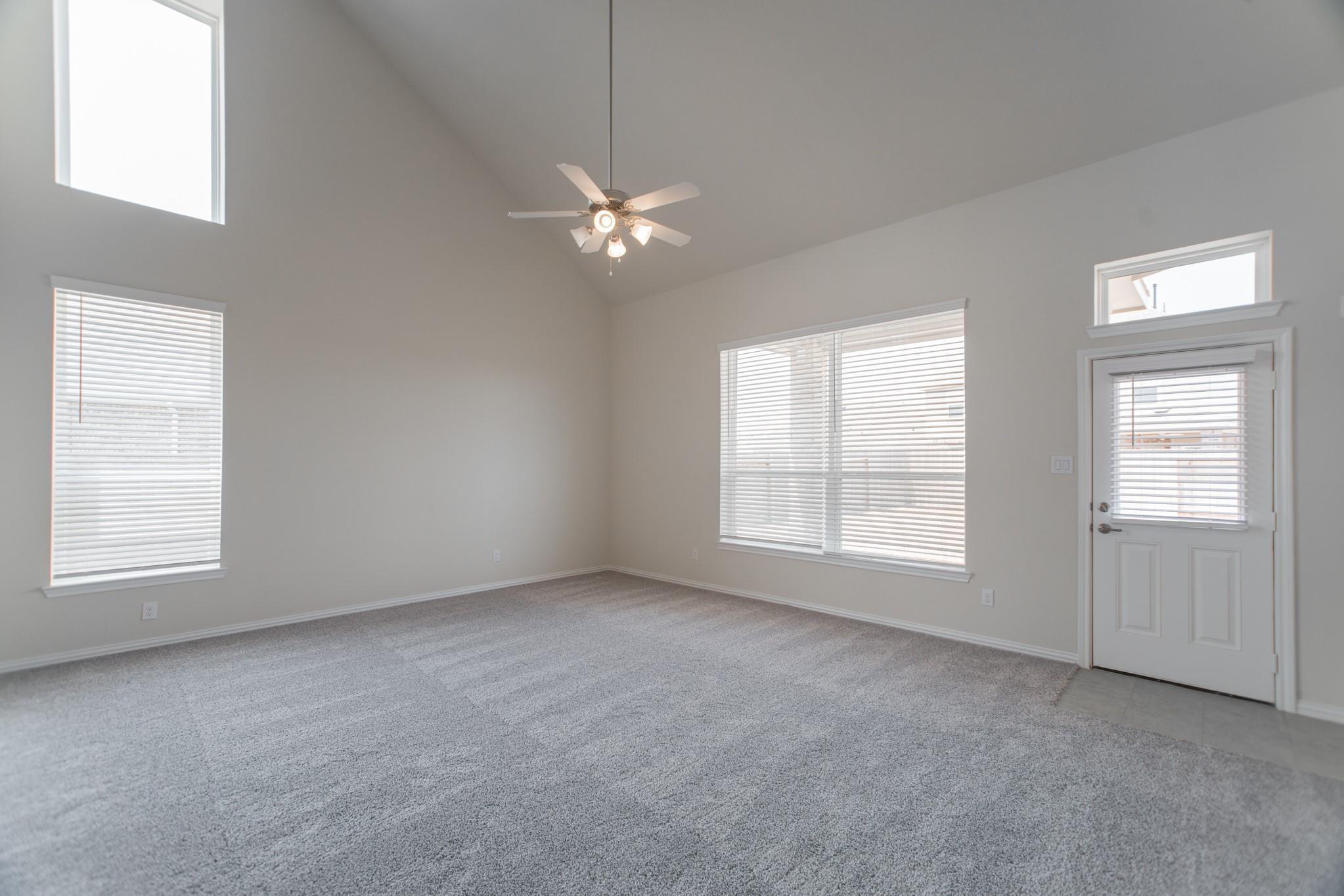 Vacant carpeted room with a vaulted ceiling, ceiling fan, and windows with blinds.