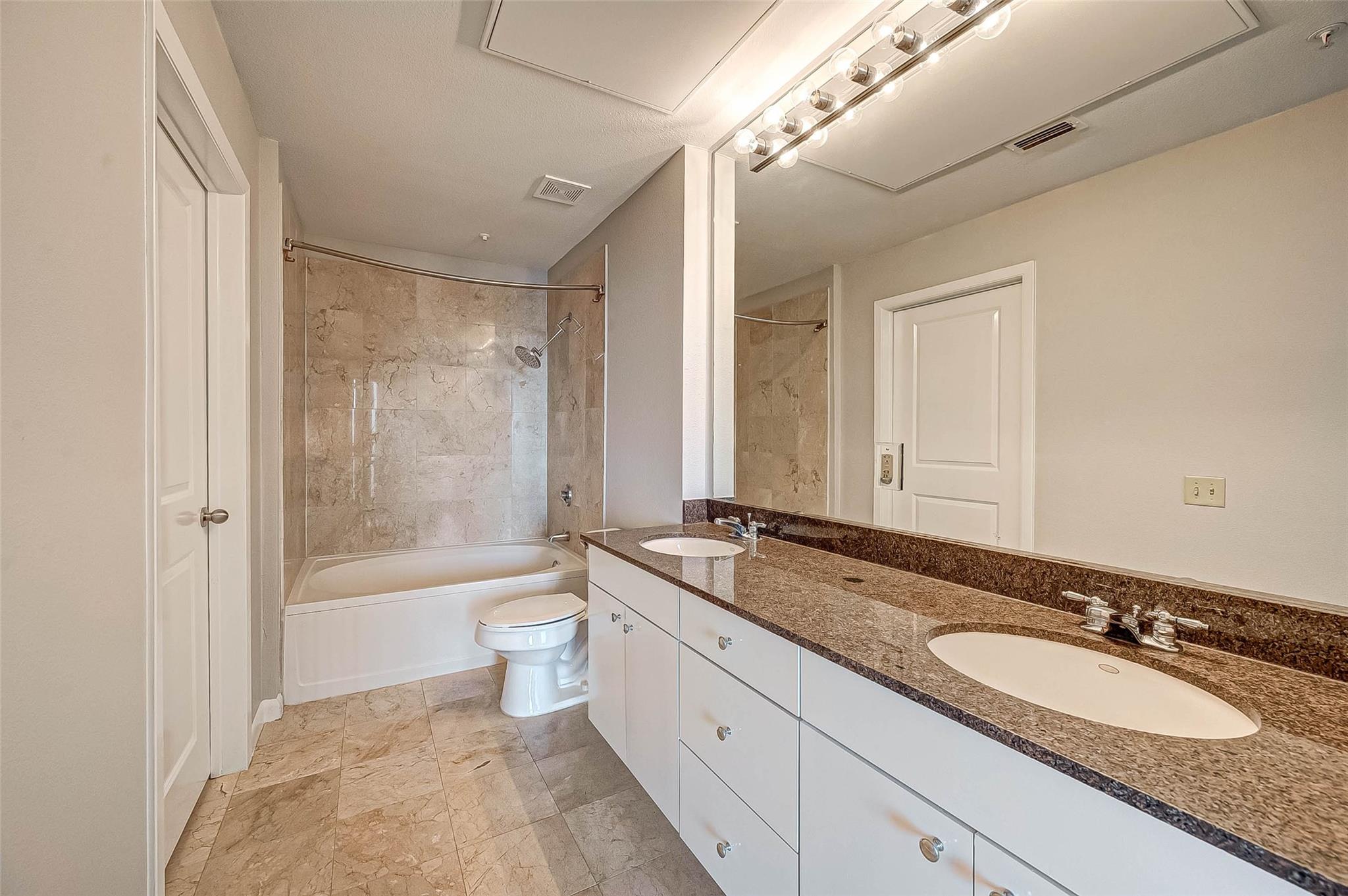 Bathroom with a tiled tub and shower and a long double-sink granite vanity.