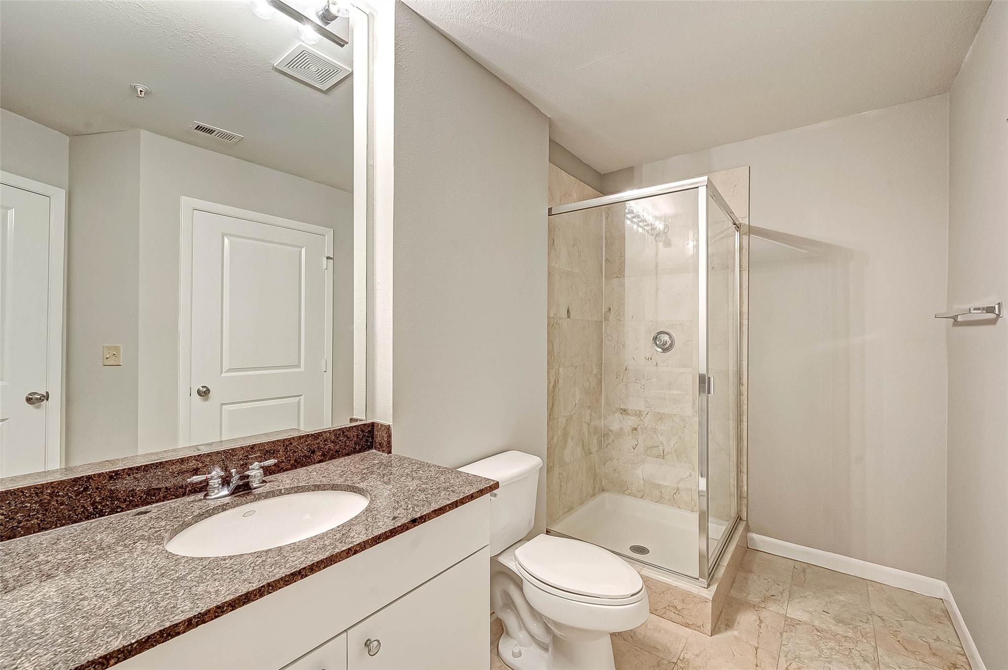 Bathroom with granite vanity, oval sink, toilet, and glass-enclosed stone-tile shower.