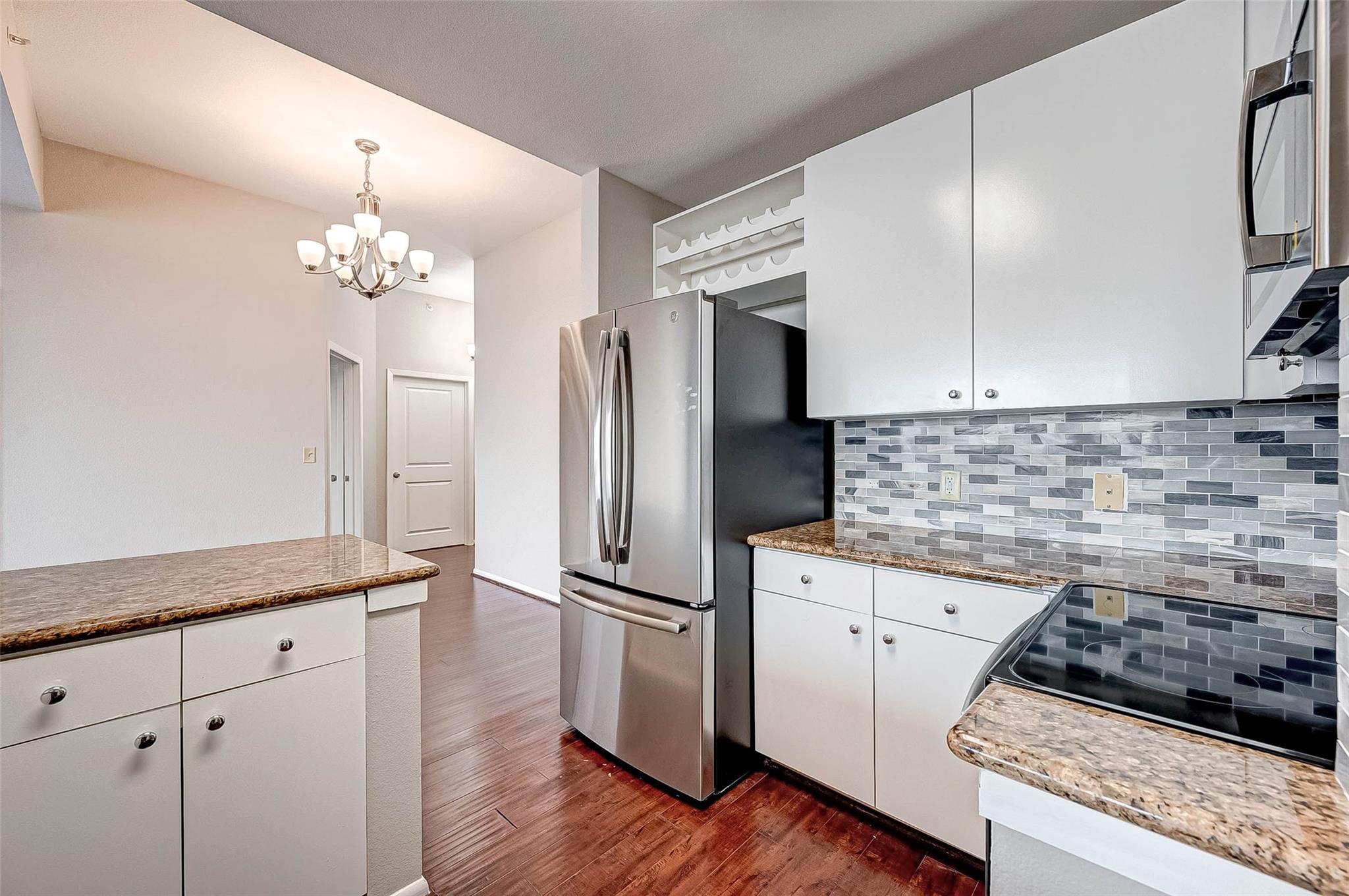 Vacant kitchen with white cabinets, stainless steel appliances, gray tile backsplash, and granite countertops.