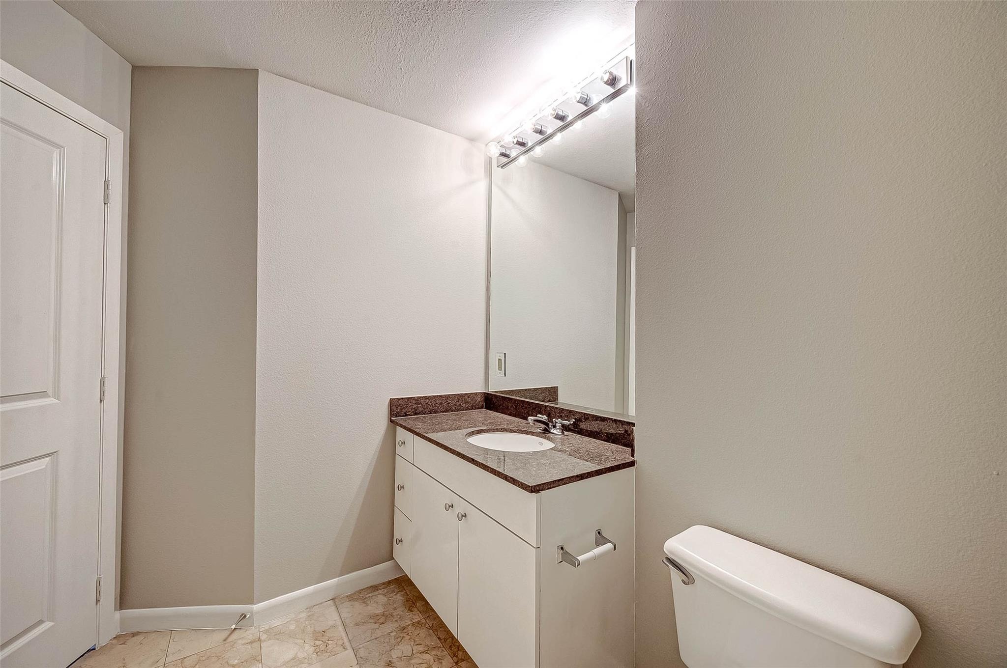 Bathroom with a granite vanity, large mirror, bright lights, and tiled floor.