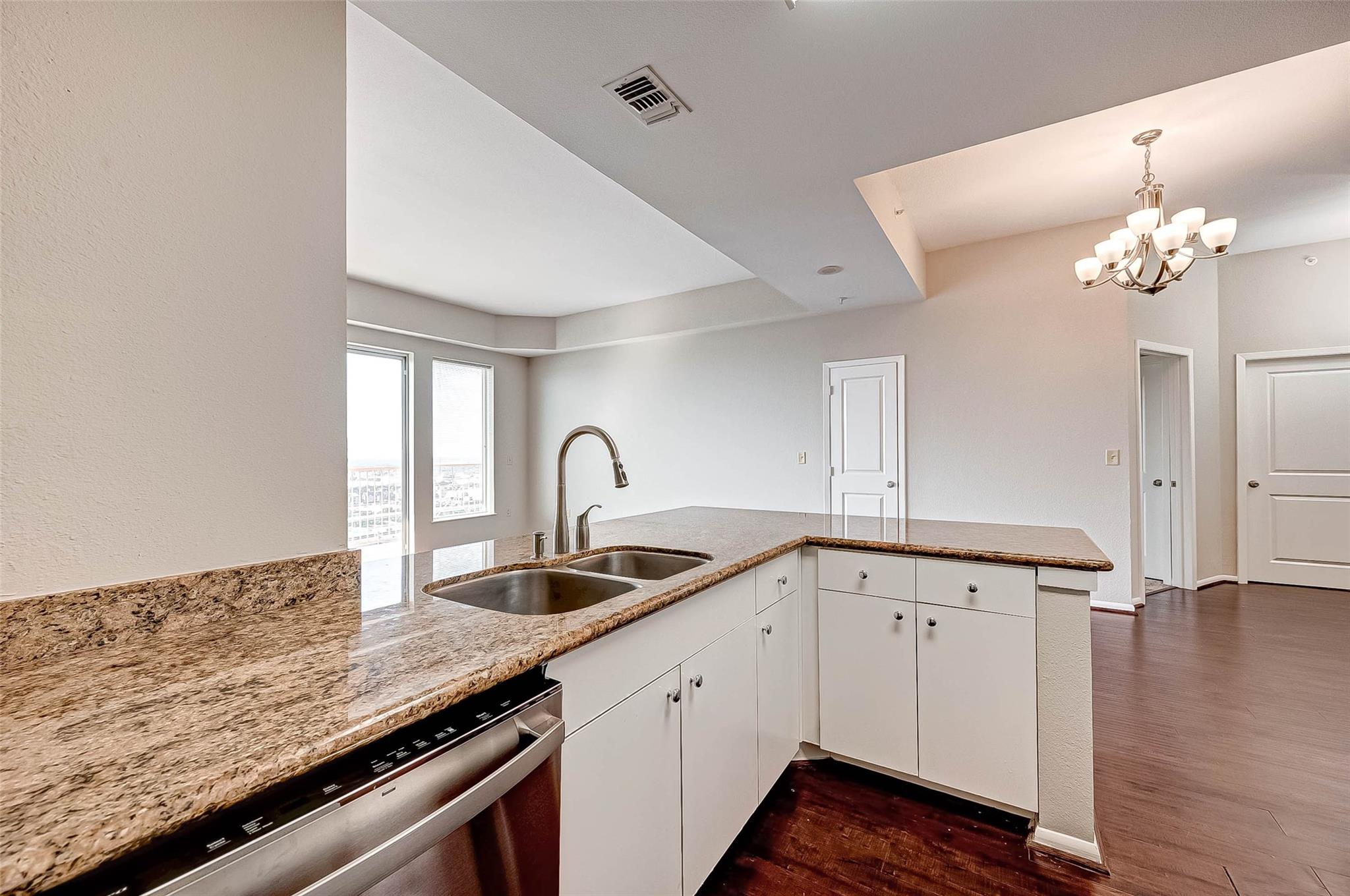 Unfurnished condo kitchen with granite counters, a double sink, stainless-steel dishwasher and adjoining open living area.