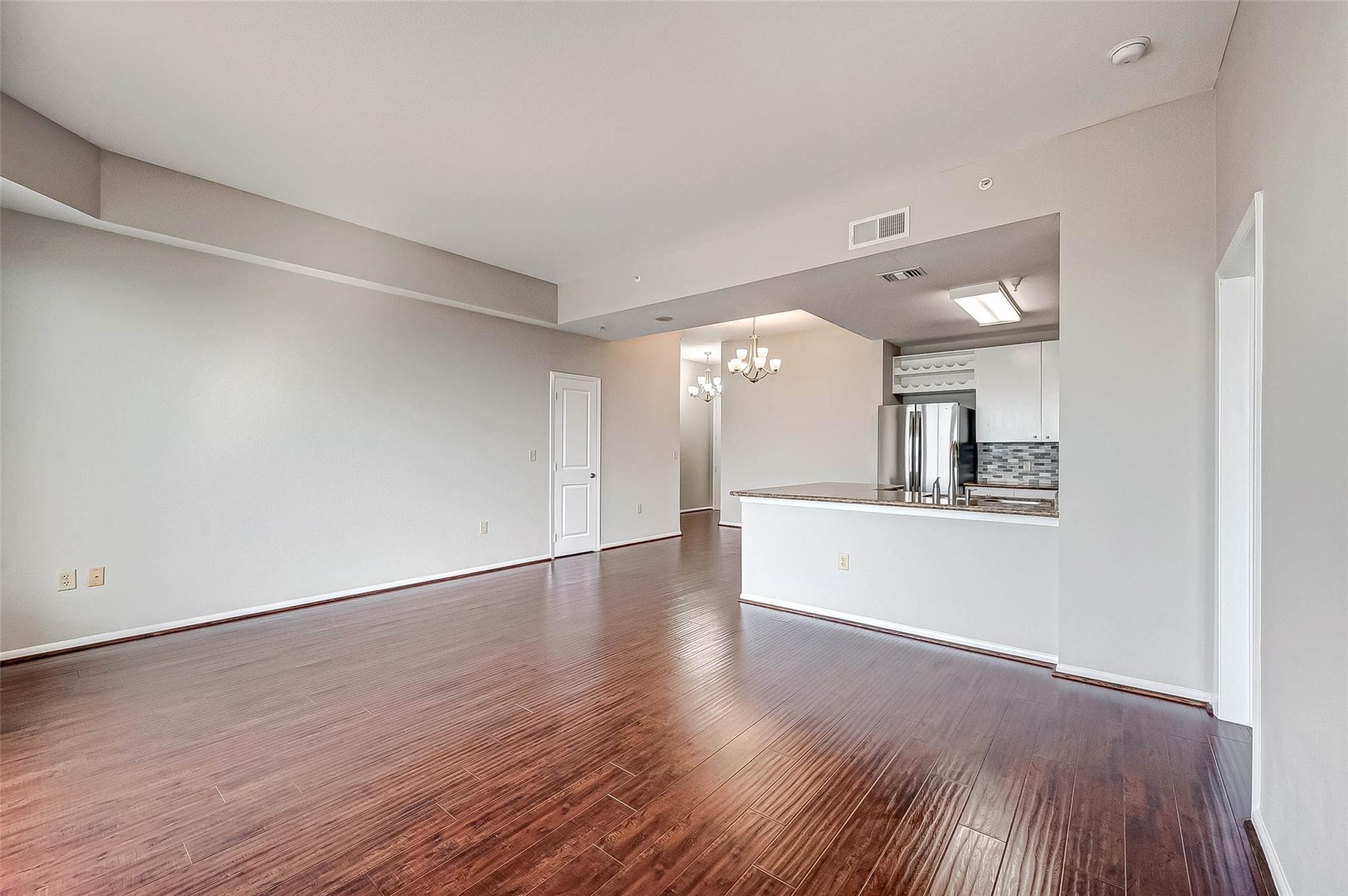 Vacant condo living area with dark plank flooring and an open kitchen pass-through.