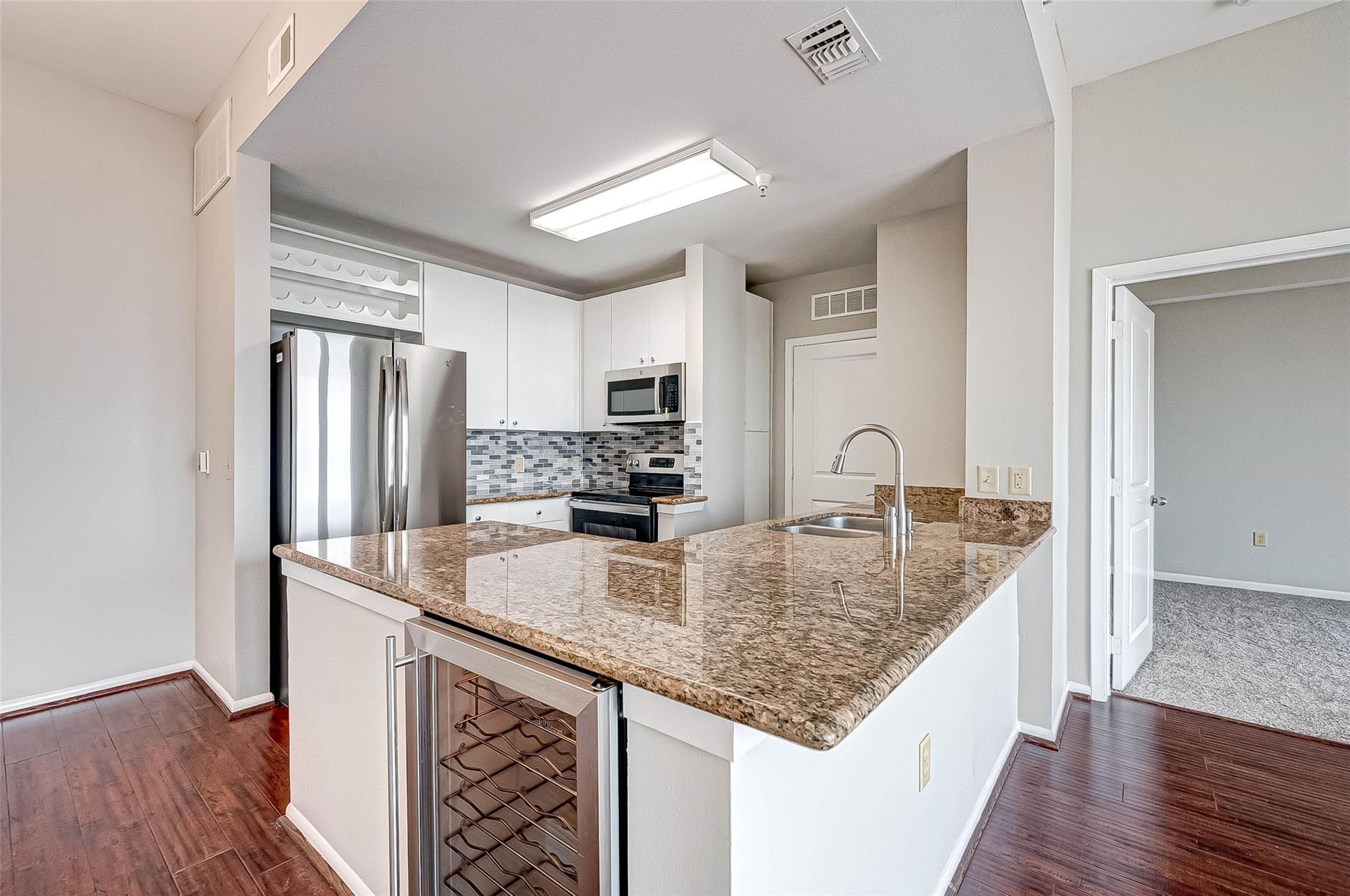 Condo kitchen with granite breakfast bar, stainless steel appliances, mosaic backsplash, and built-in wine rack.