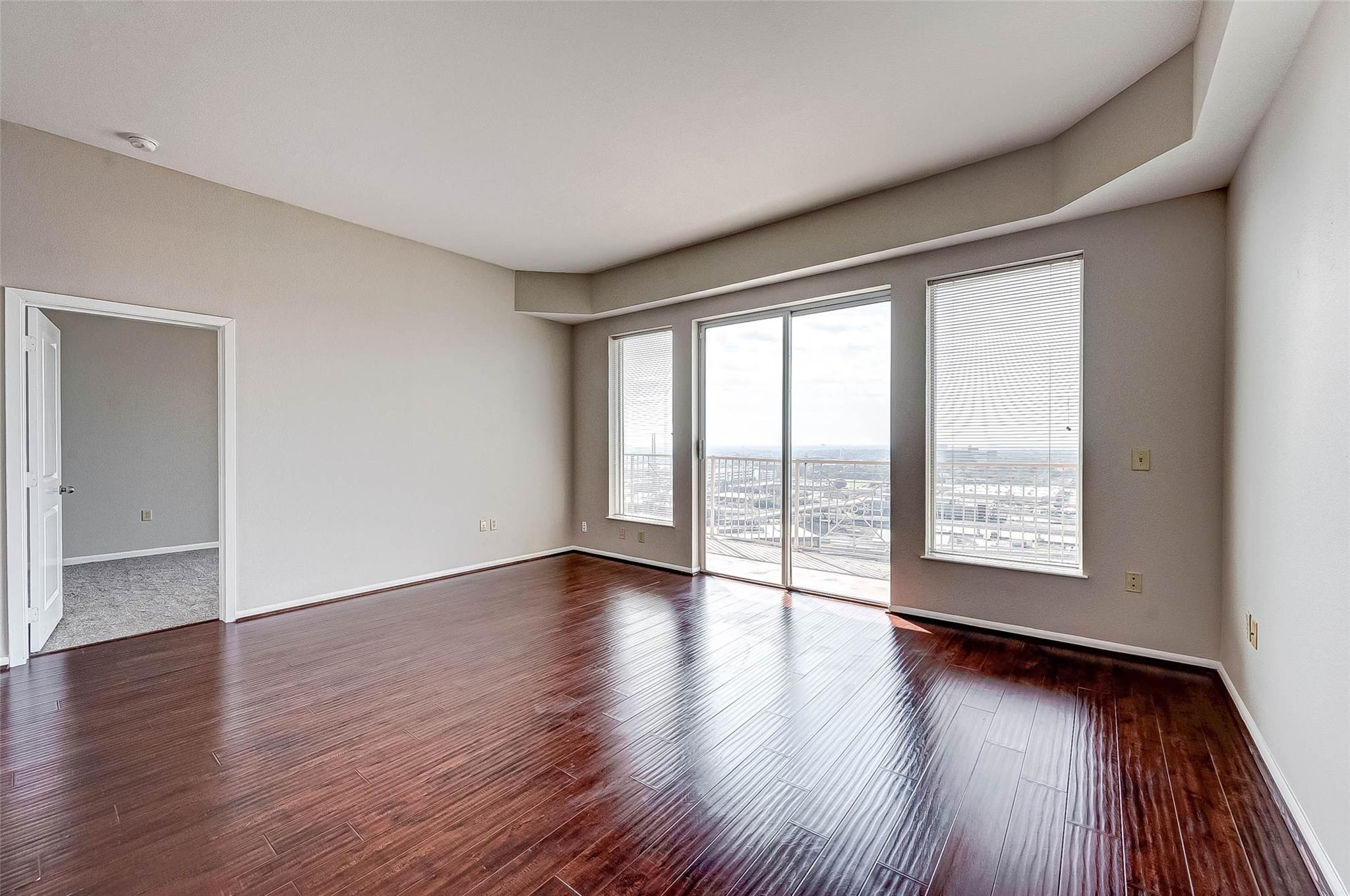 Vacant living room with glossy dark floors, large windows, and a sliding glass door to a balcony.