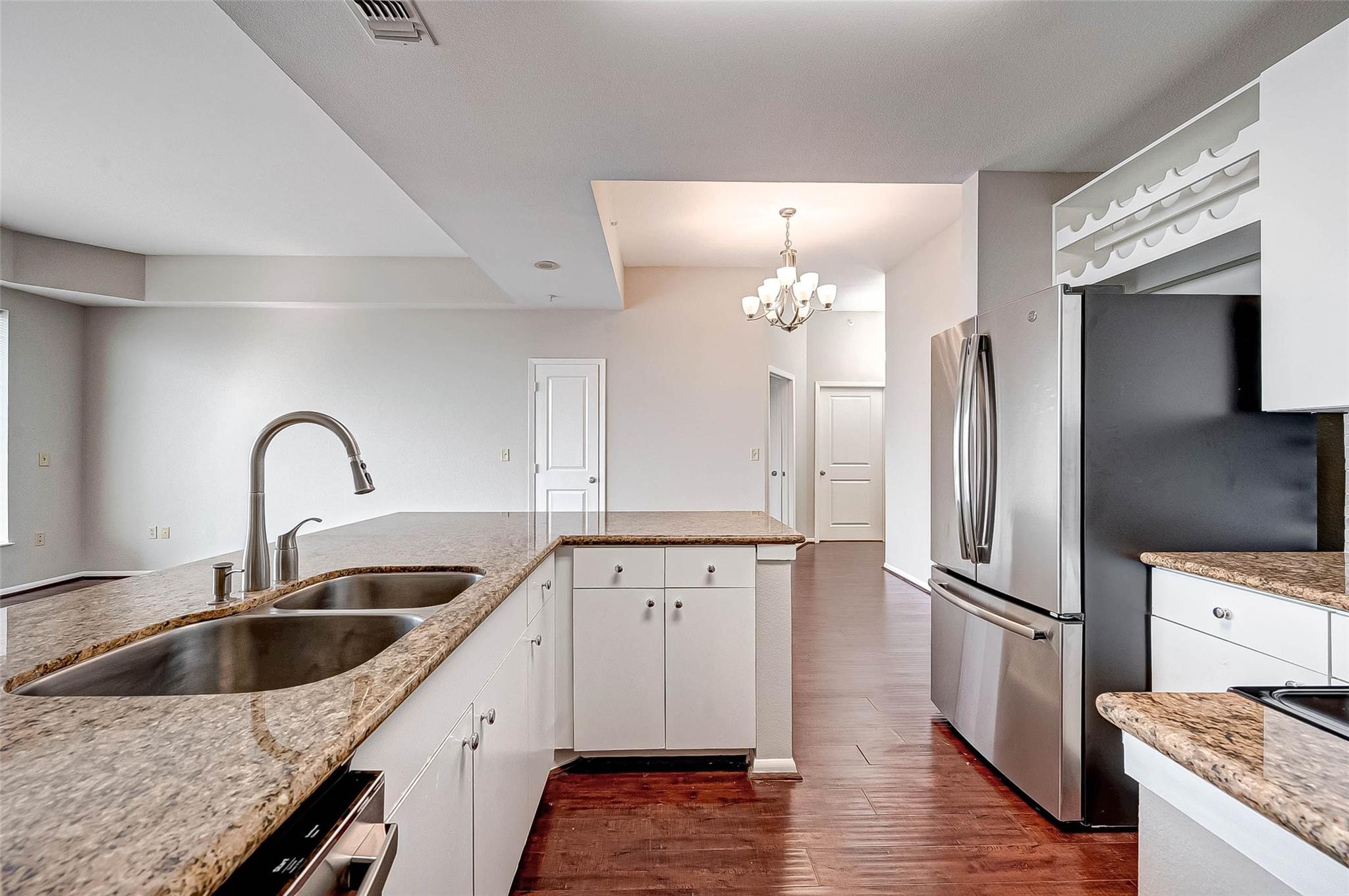 Kitchen with granite counters, a double sink, white cabinets, stainless steel refrigerator, and dark wood floors.