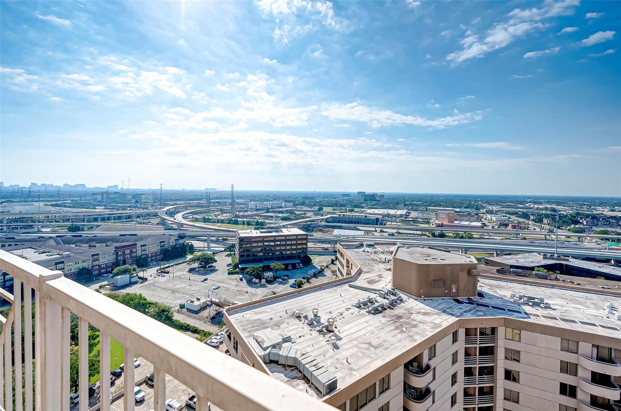 High-rise balcony view over Houston rooftops and intersecting highways beneath a wide blue sky.
