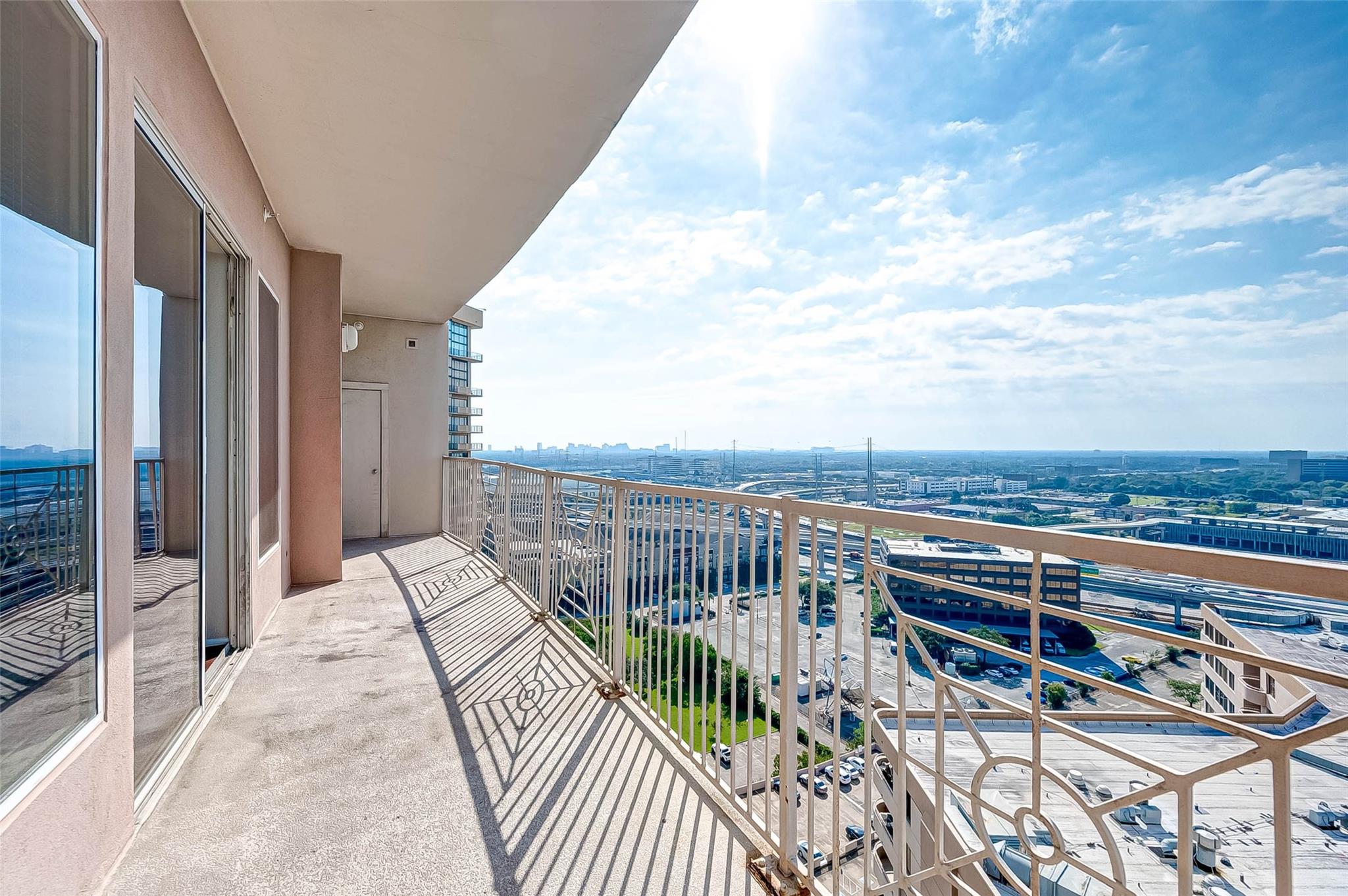 High-rise apartment balcony overlooking Houston, with a covered ceiling and metal railing.