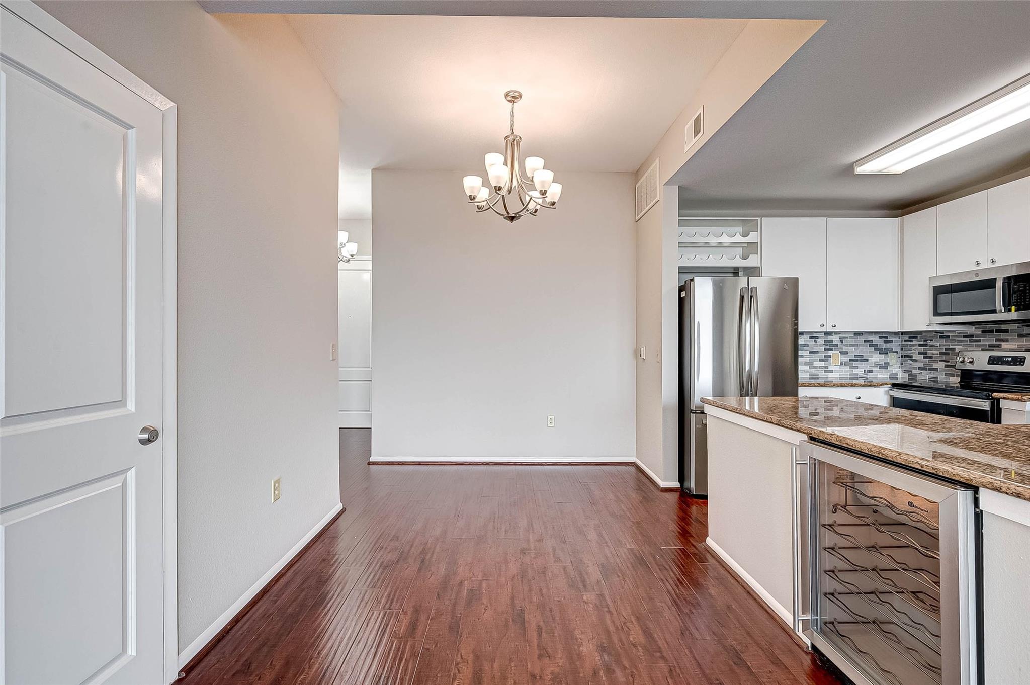 Unfurnished dining area beside a modern kitchen with a granite island and built-in wine rack.
