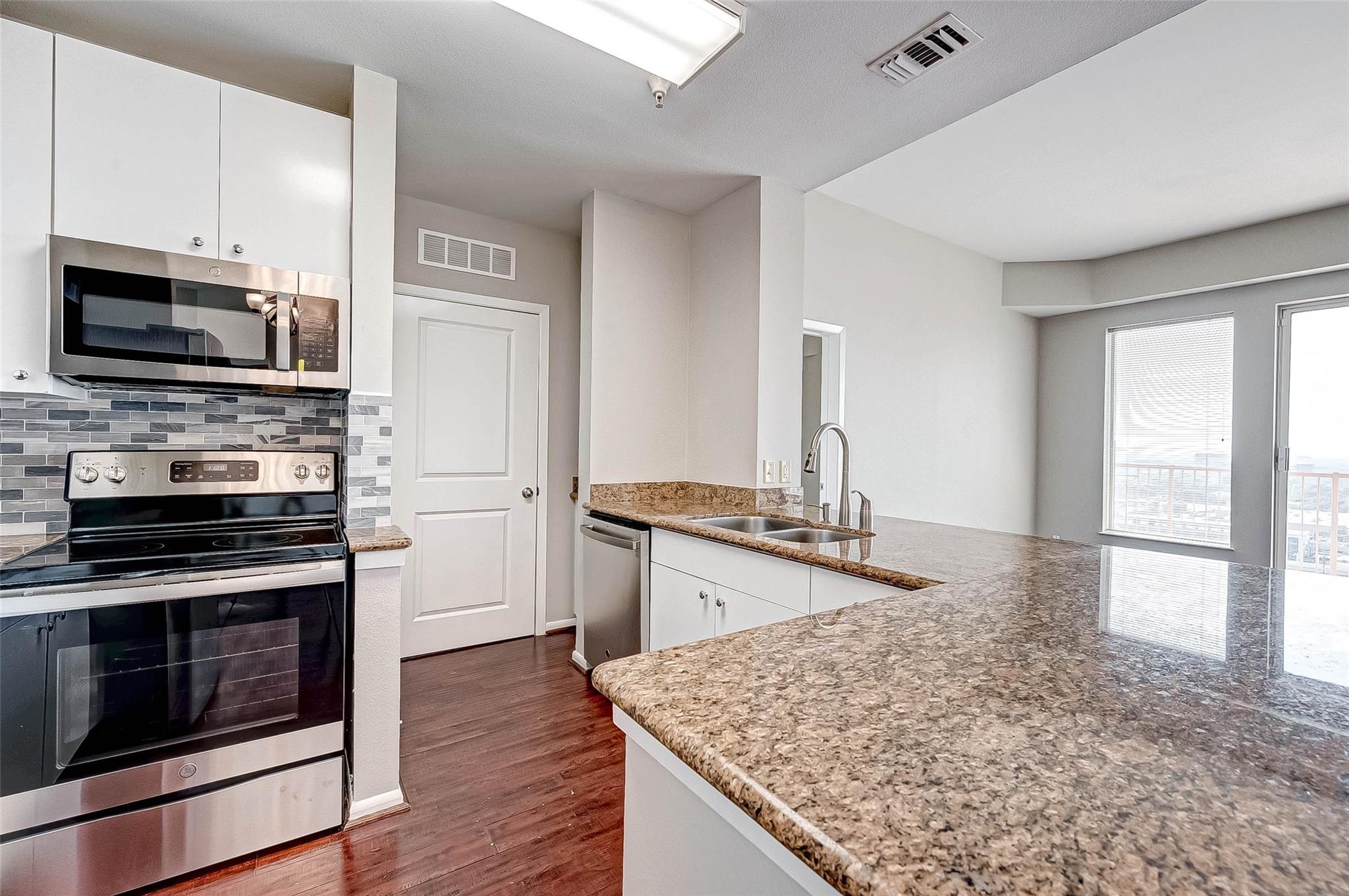 Condominium kitchen with granite counters, stainless steel appliances, and a balcony door.