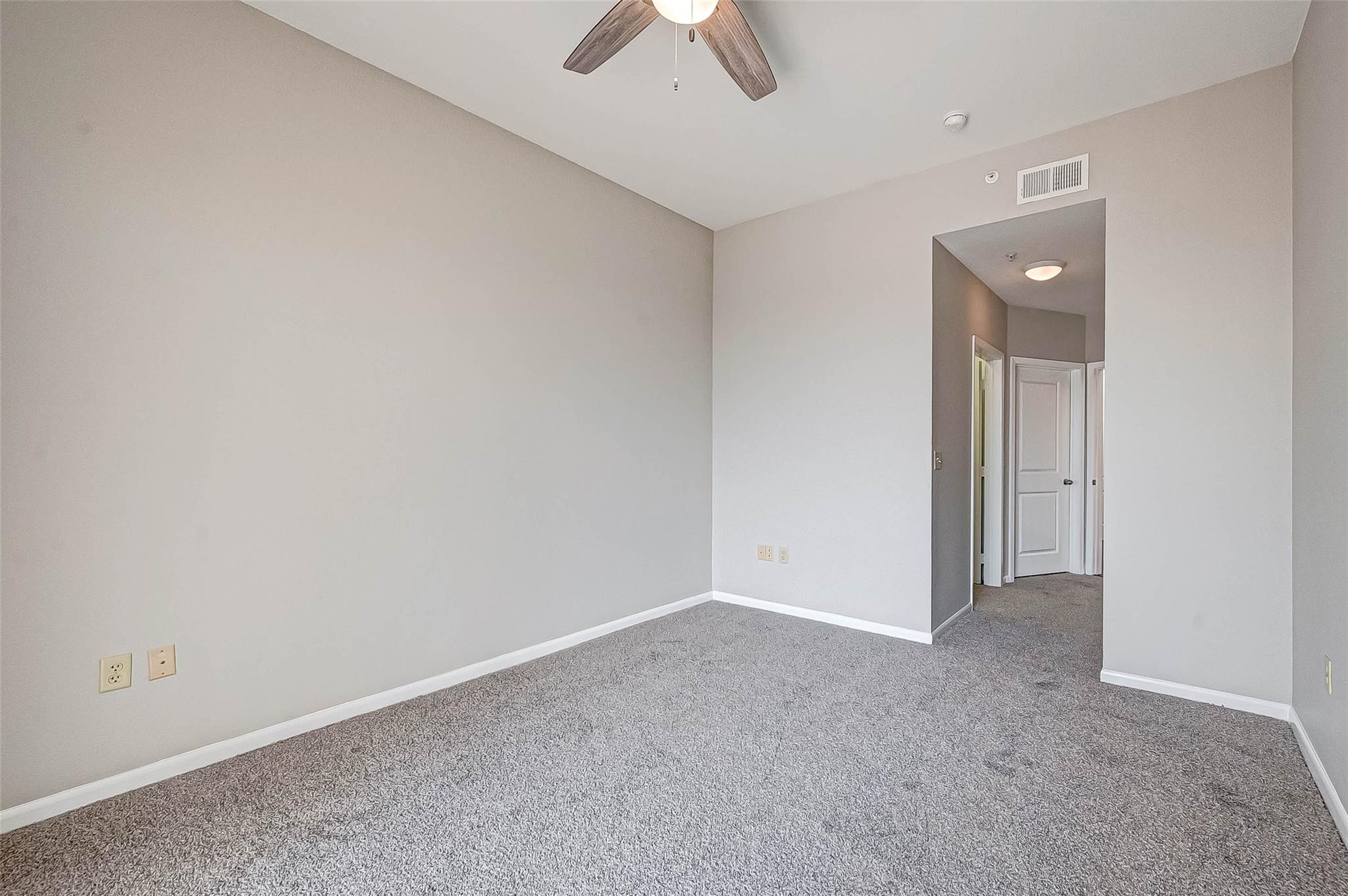Empty bedroom with gray carpet and a ceiling fan, viewed toward the hallway.