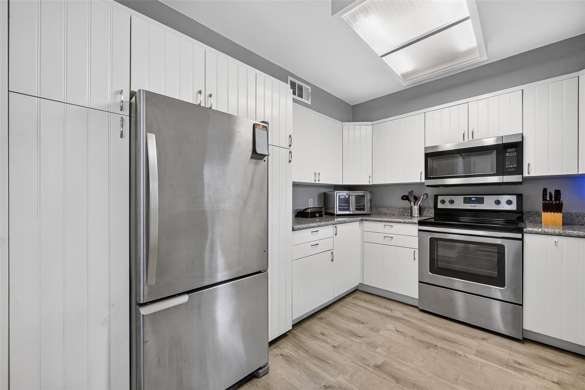 Kitchen with white cabinetry, stainless-steel appliances, and wood-look flooring.