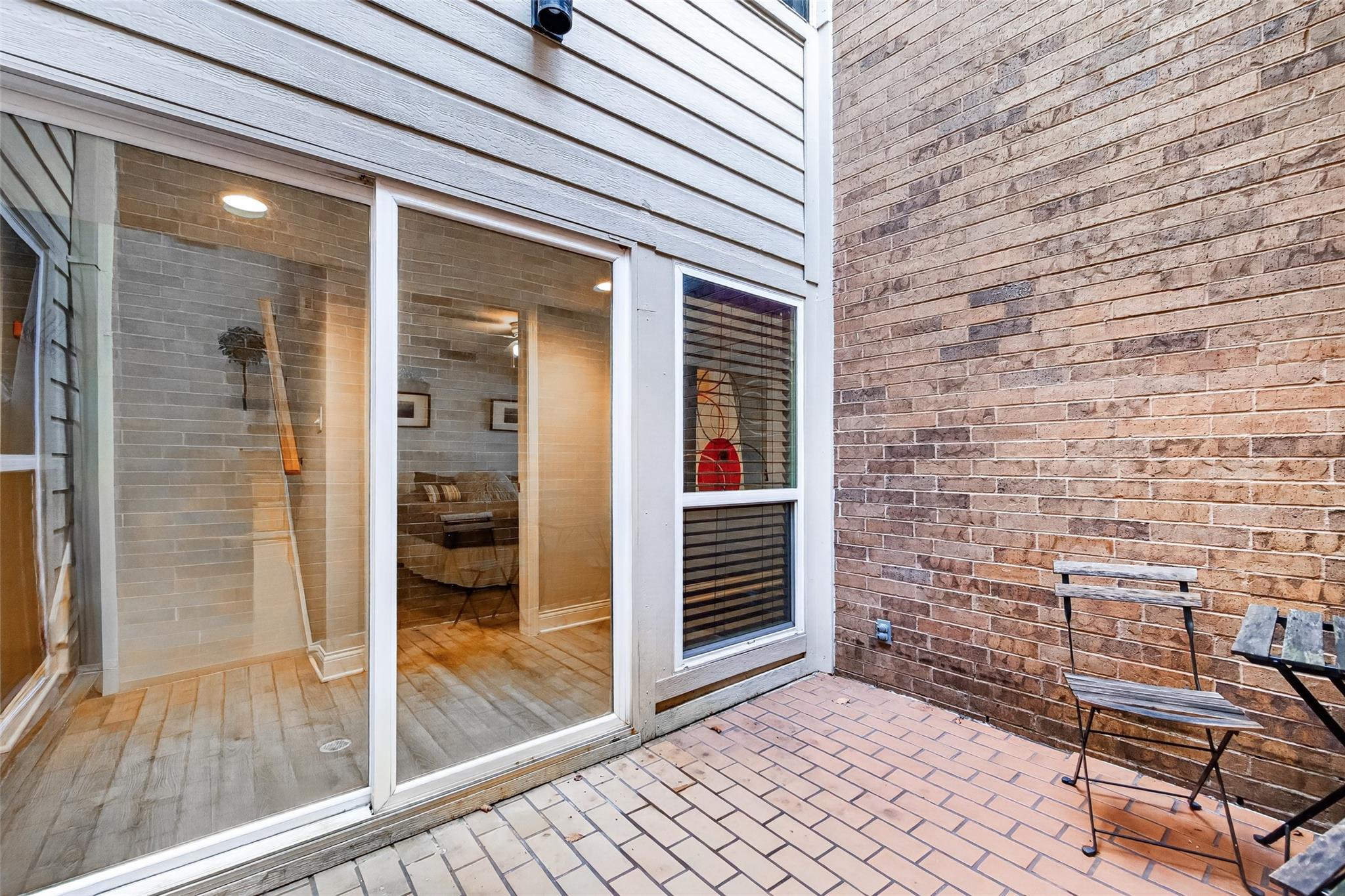 Private brick patio with metal chairs beside a sliding glass door.