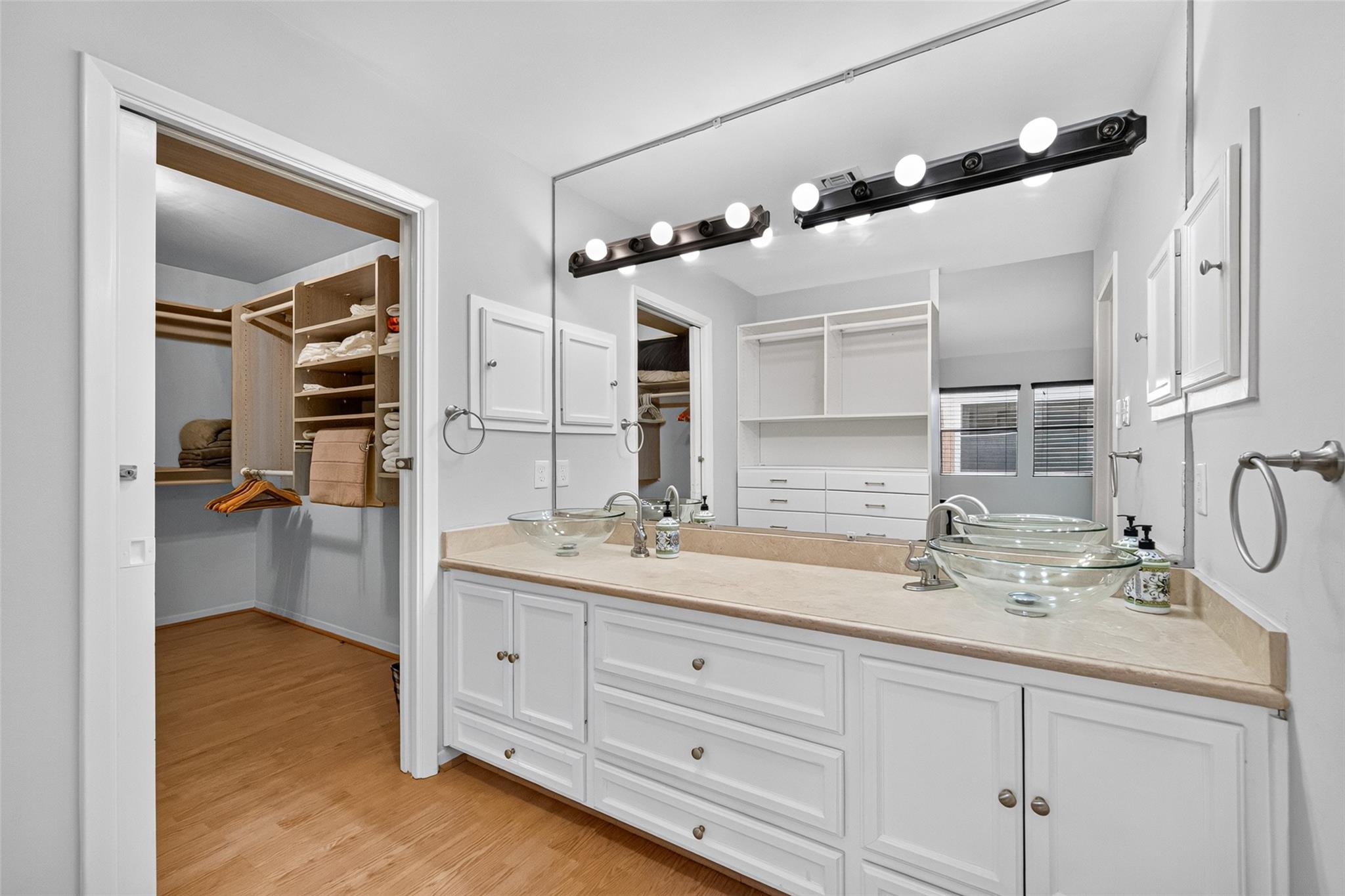 Bathroom with double glass vessel sinks and a walk-in closet with built-in wooden shelving.