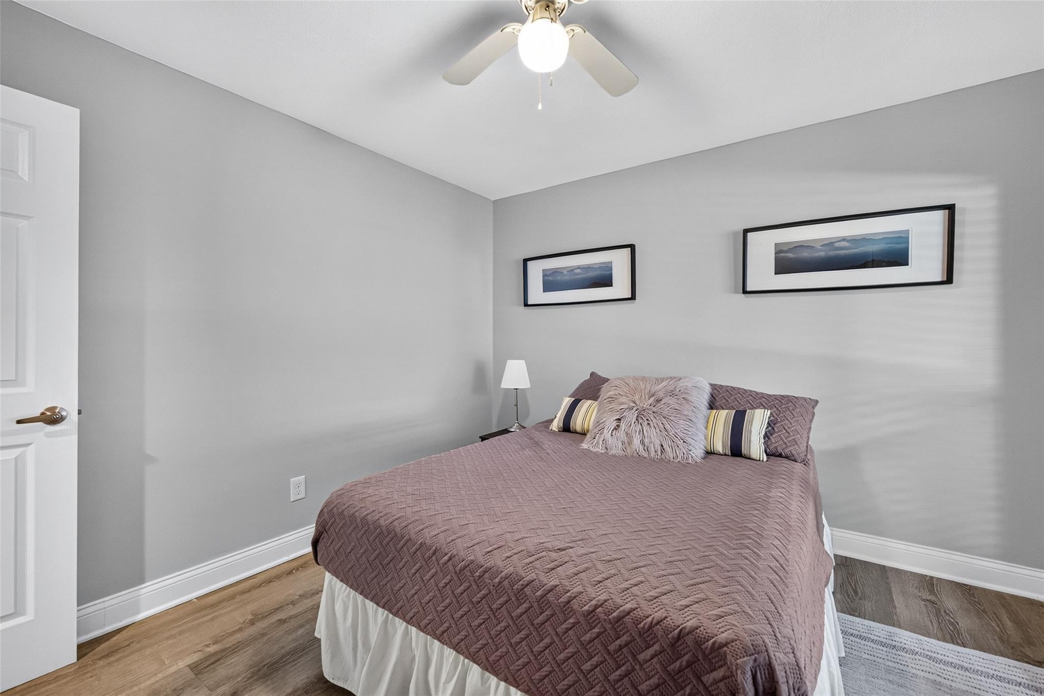 Bedroom with a mauve quilted bed, striped pillows, gray walls, and framed landscape prints.