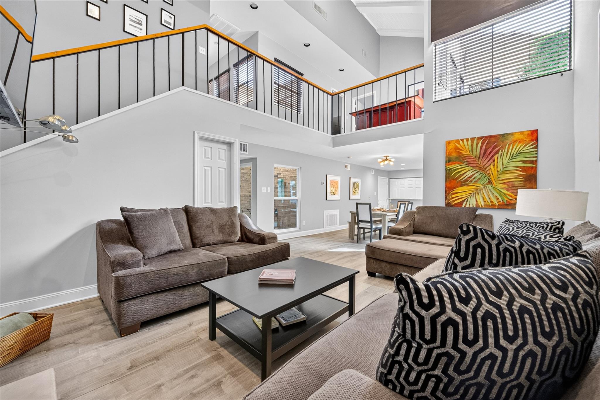 Staged living room with a mezzanine loft, vaulted ceiling, and open dining area.