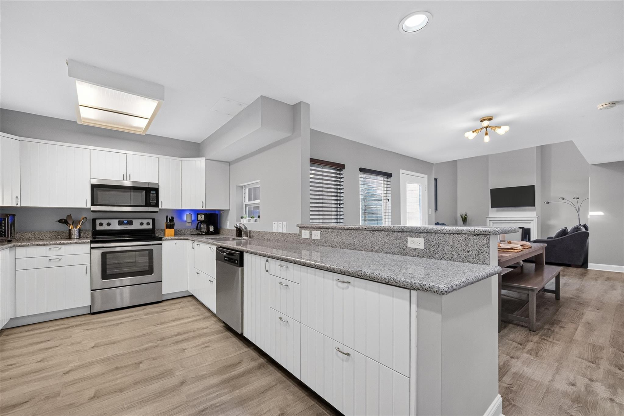Open-plan kitchen with white cabinets, stainless steel appliances, granite counters, and an adjoining living area.