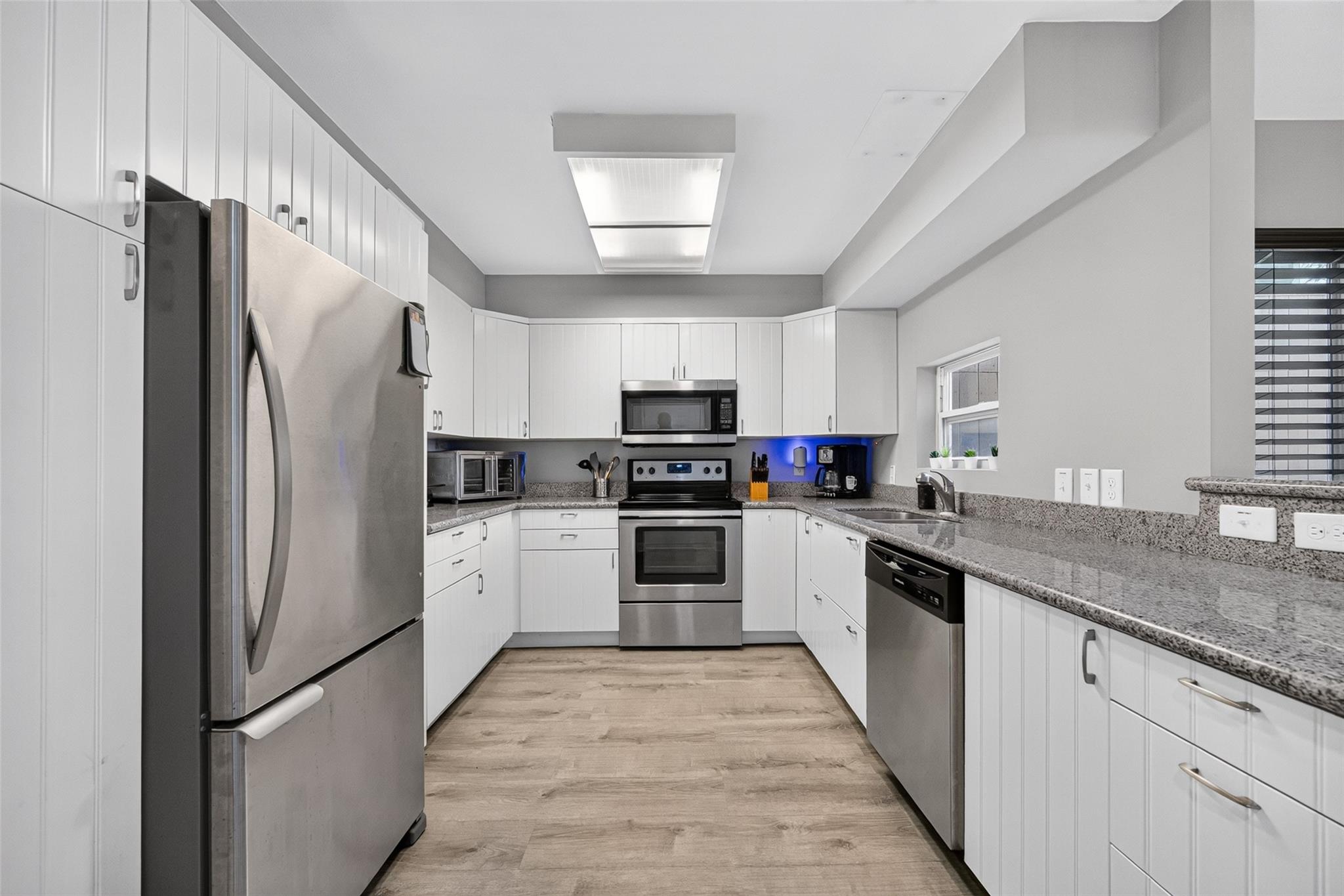 Modern kitchen with white cabinets, granite counters, stainless steel appliances, and wood-look flooring.