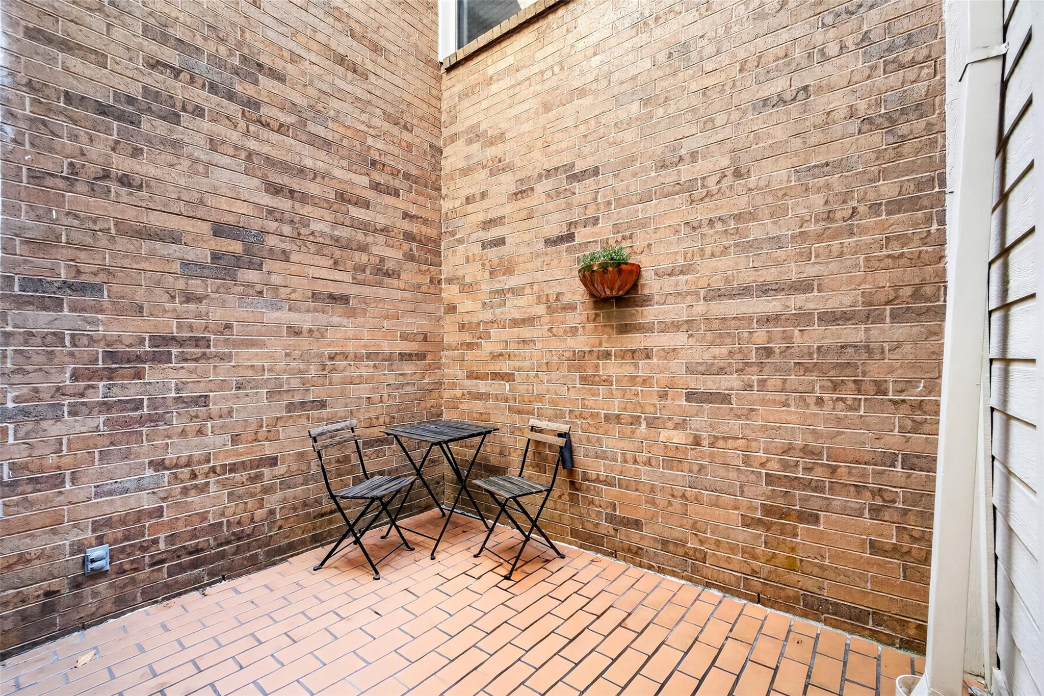 Brick patio with terracotta paving, a small café table and two folding chairs.