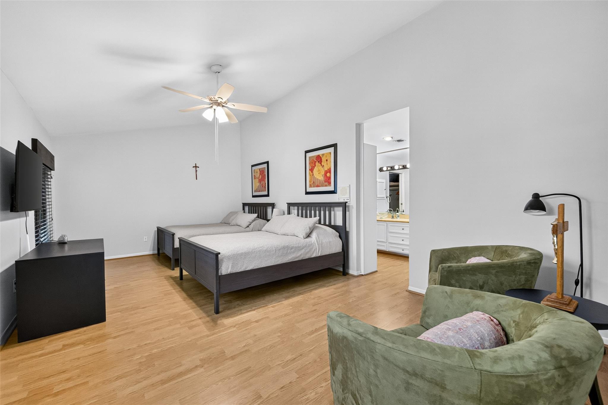 Furnished bedroom with a dark wood bed, hardwood floors, and green chairs beside the ensuite doorway.