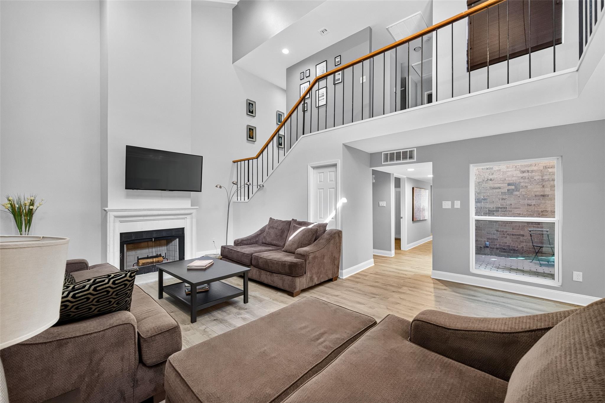 Living room with a tall staircase, fireplace, wall-mounted TV, and brown seating.