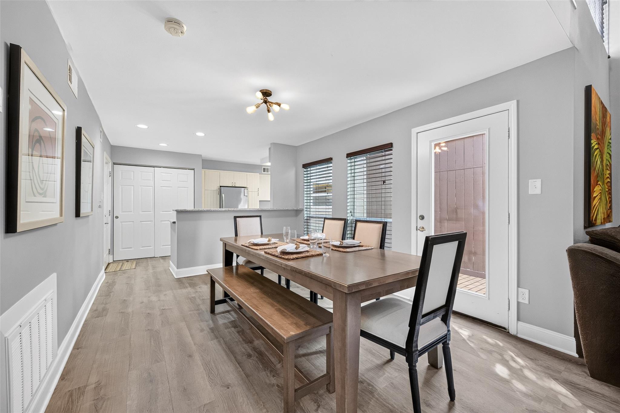 Dining area with a wooden table and bench beside a glass patio door, open to the kitchen.