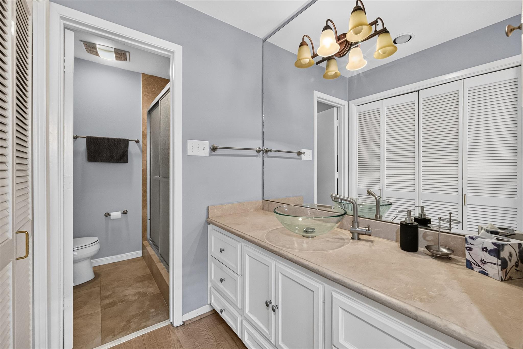 Bathroom vanity with a glass vessel sink beside an adjoining shower and toilet area.