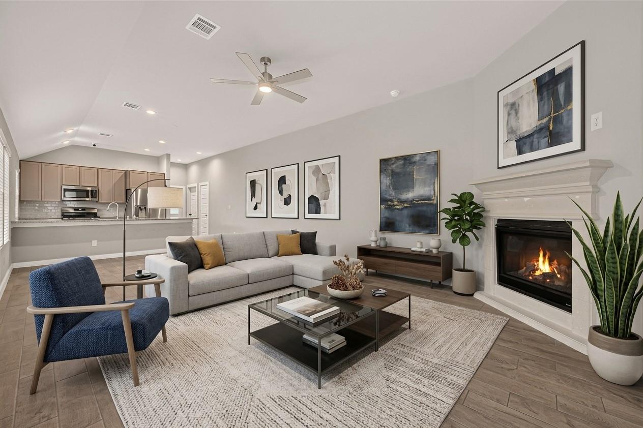Living room with a gray sectional, blue accent chair, and lit fireplace beside an open kitchen.