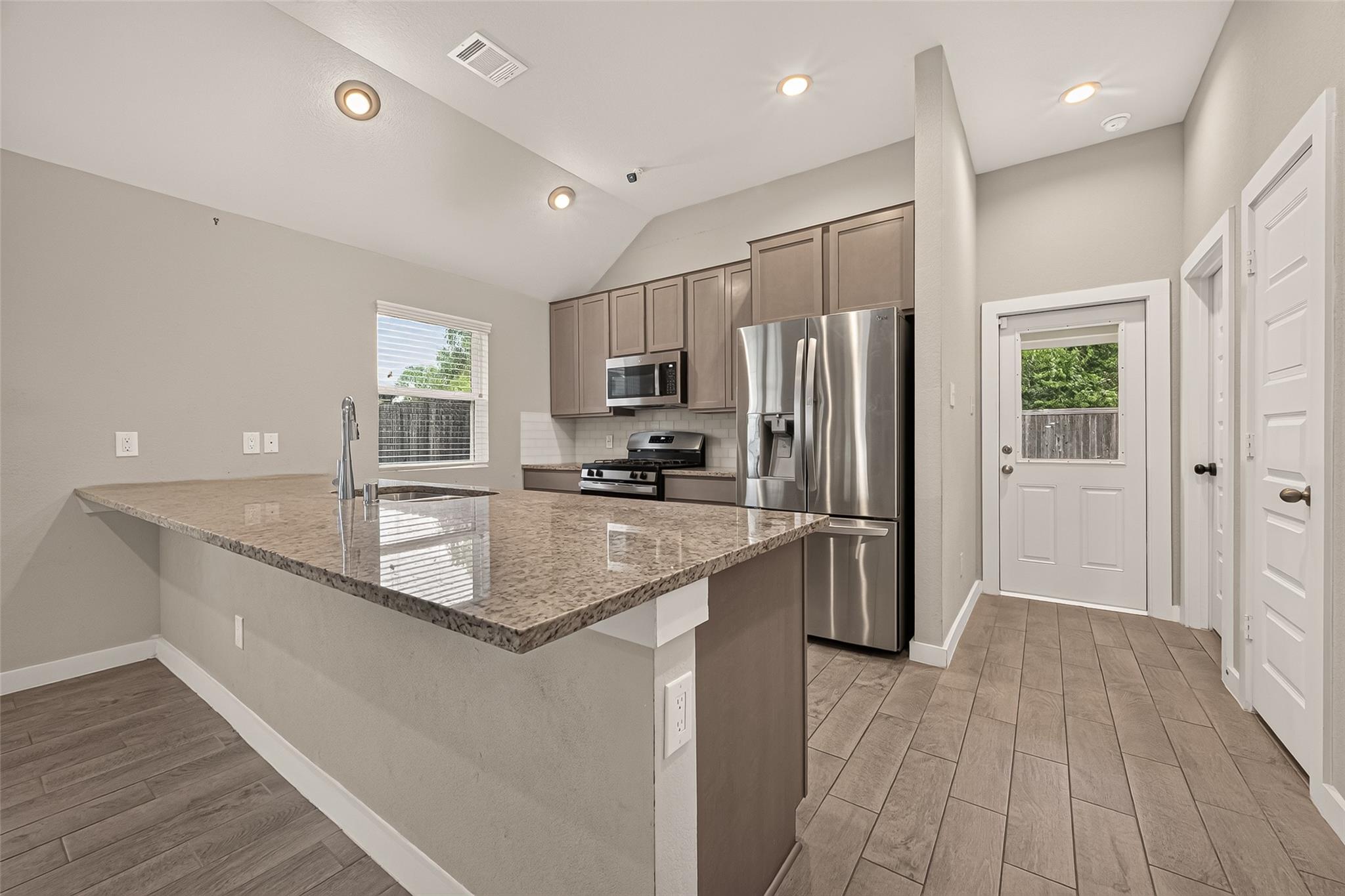 Kitchen with a large granite island, taupe cabinets, and stainless steel appliances.