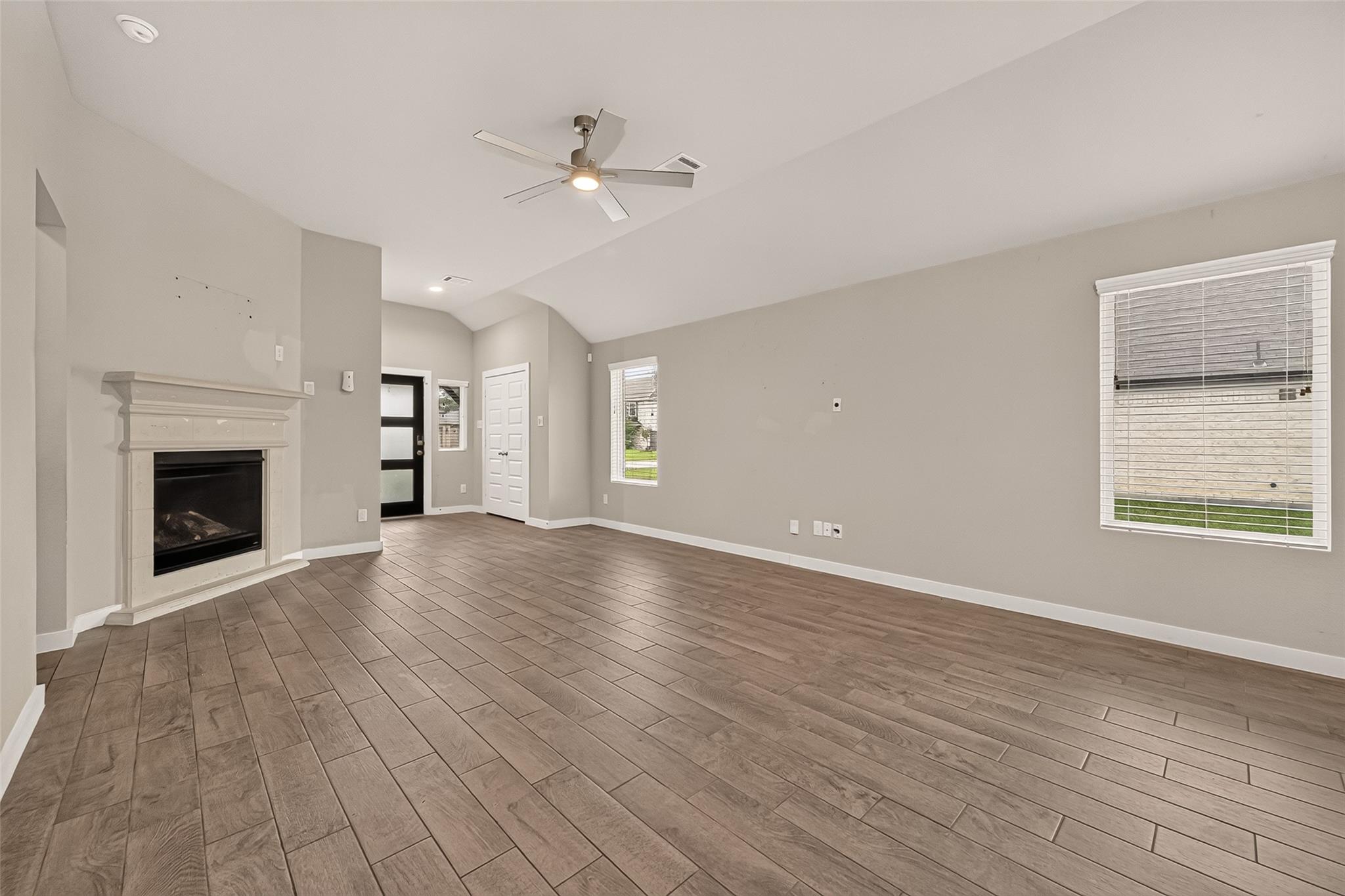 Empty living room with a white fireplace, wood-look tile floors, and ceiling fan.