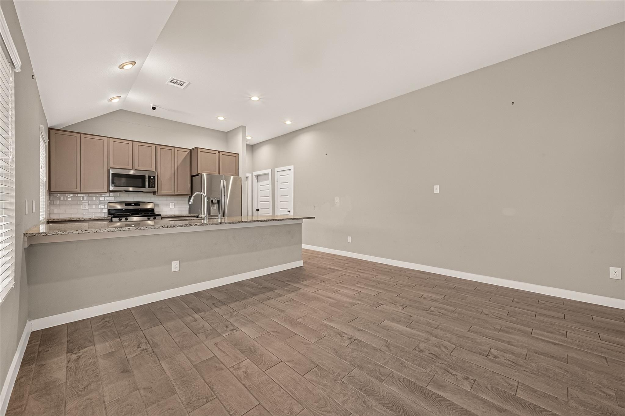 Vacant kitchen with brown cabinets, stainless steel appliances, breakfast bar, and wood-look tile flooring.