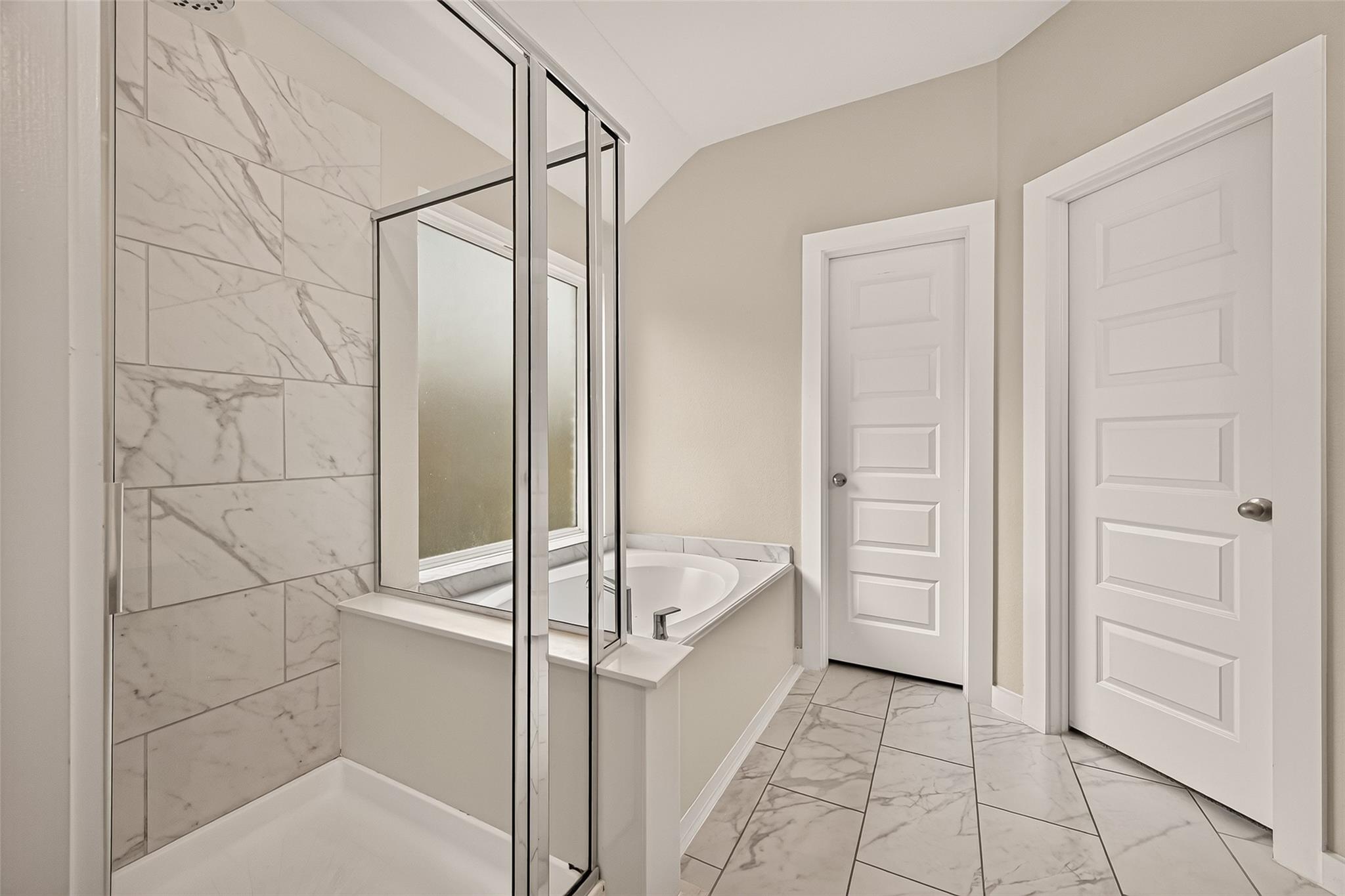 Bathroom with a glass shower, marble-look tile, and a built-in soaking tub beneath a window.