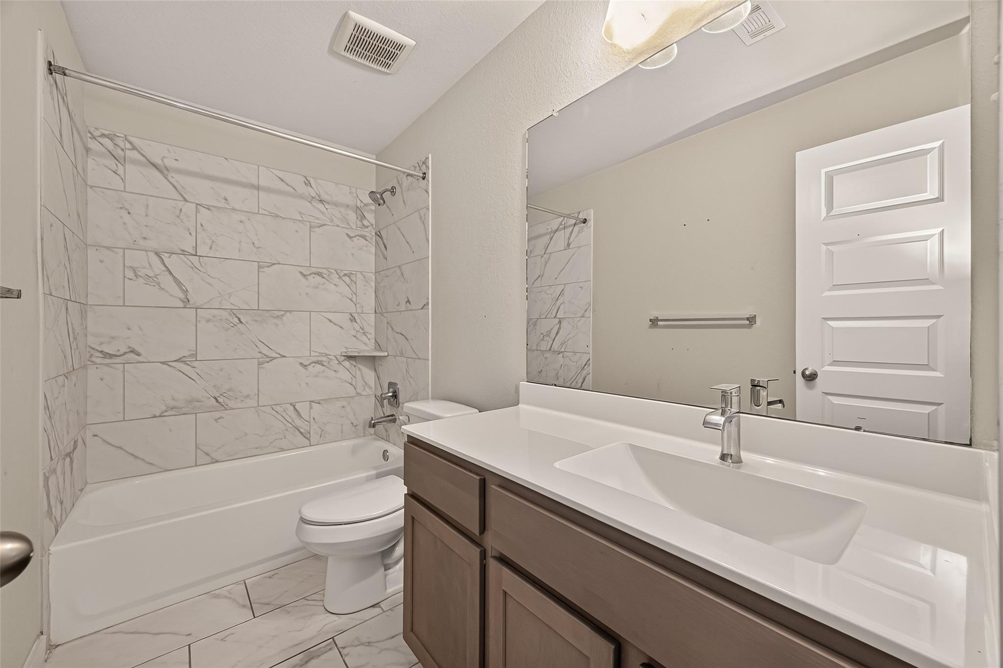 Bathroom with marble-look tile around the tub and a brown vanity with a wide white sink.