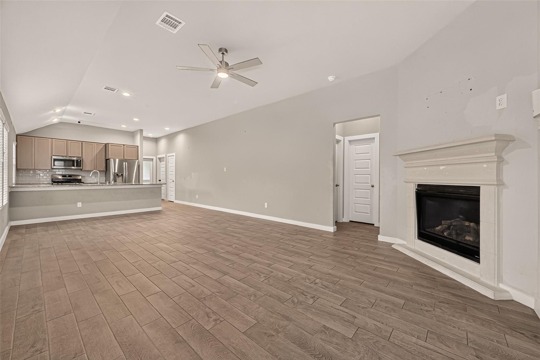 Vacant open-plan living room and kitchen with a white fireplace and wood-look tile flooring.