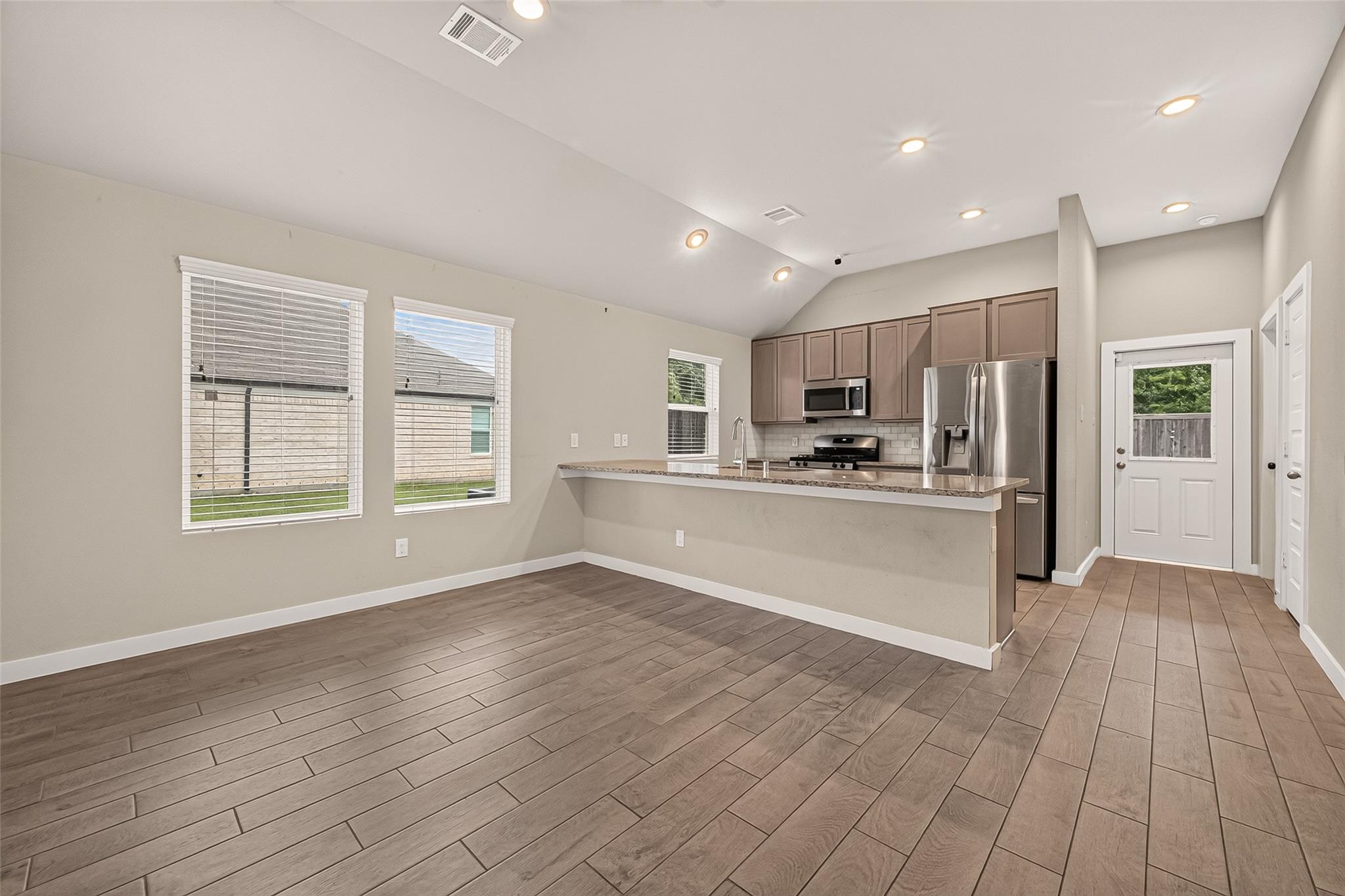 Empty dining area opens to a kitchen with a breakfast bar and stainless steel appliances.