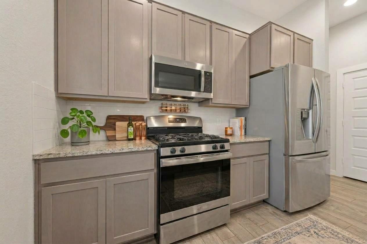 Kitchen with taupe cabinets, stainless steel appliances, and a gas range beneath a microwave.