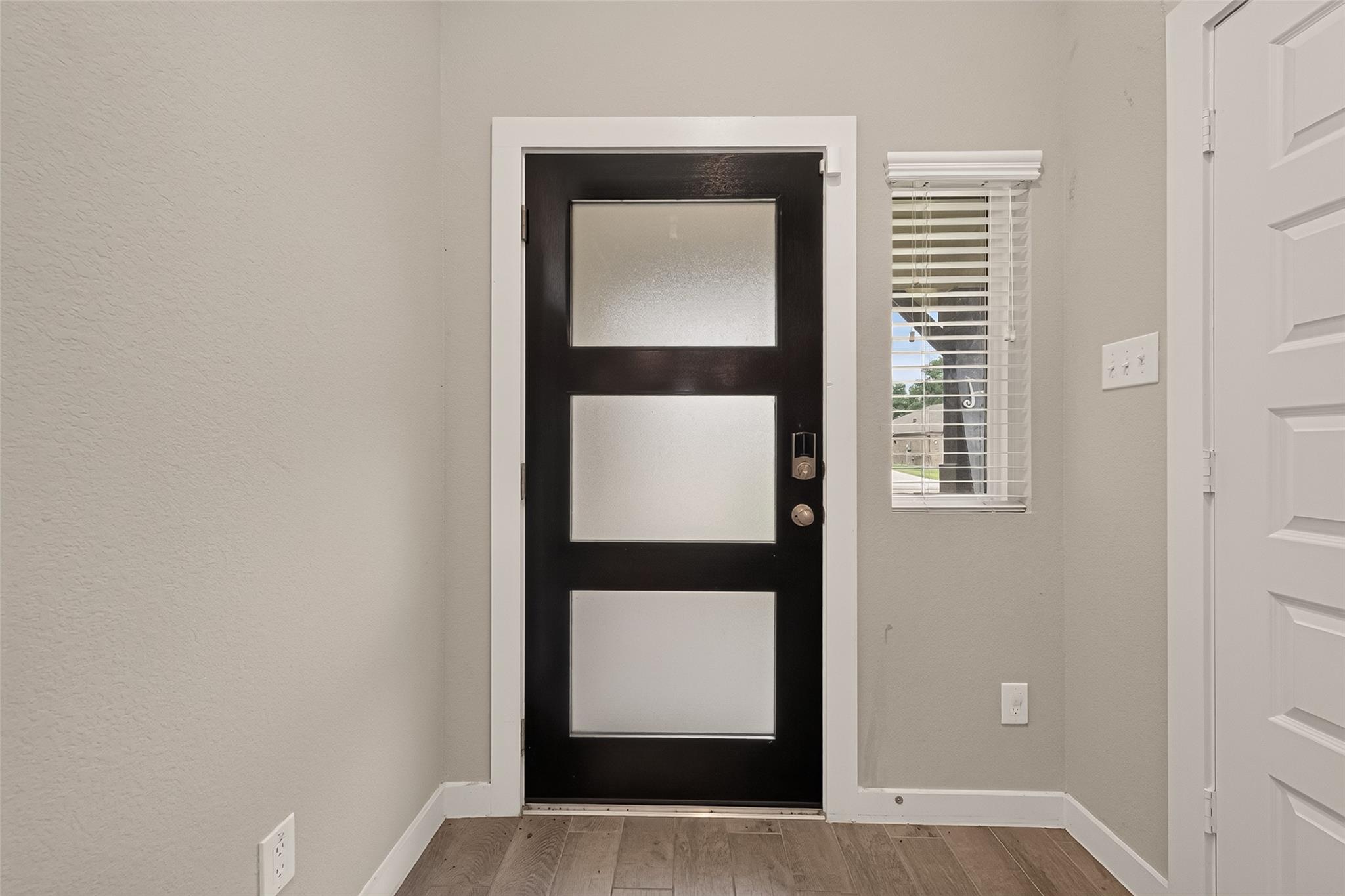 Entryway with a black frosted-glass front door, window blinds, and wood-look tile floor.