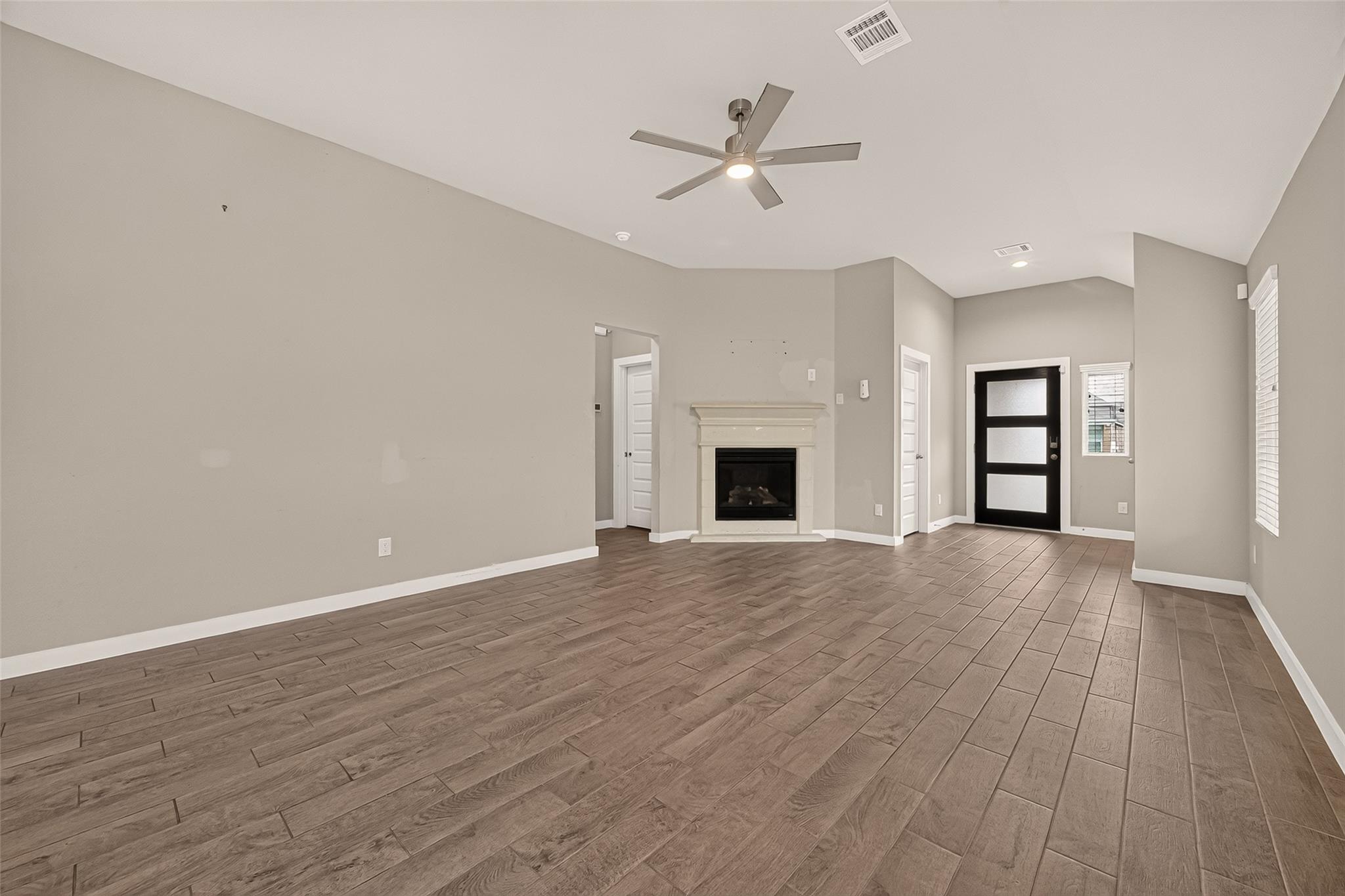 Empty living room with a white fireplace, wood-look tile floors, and a black front door.