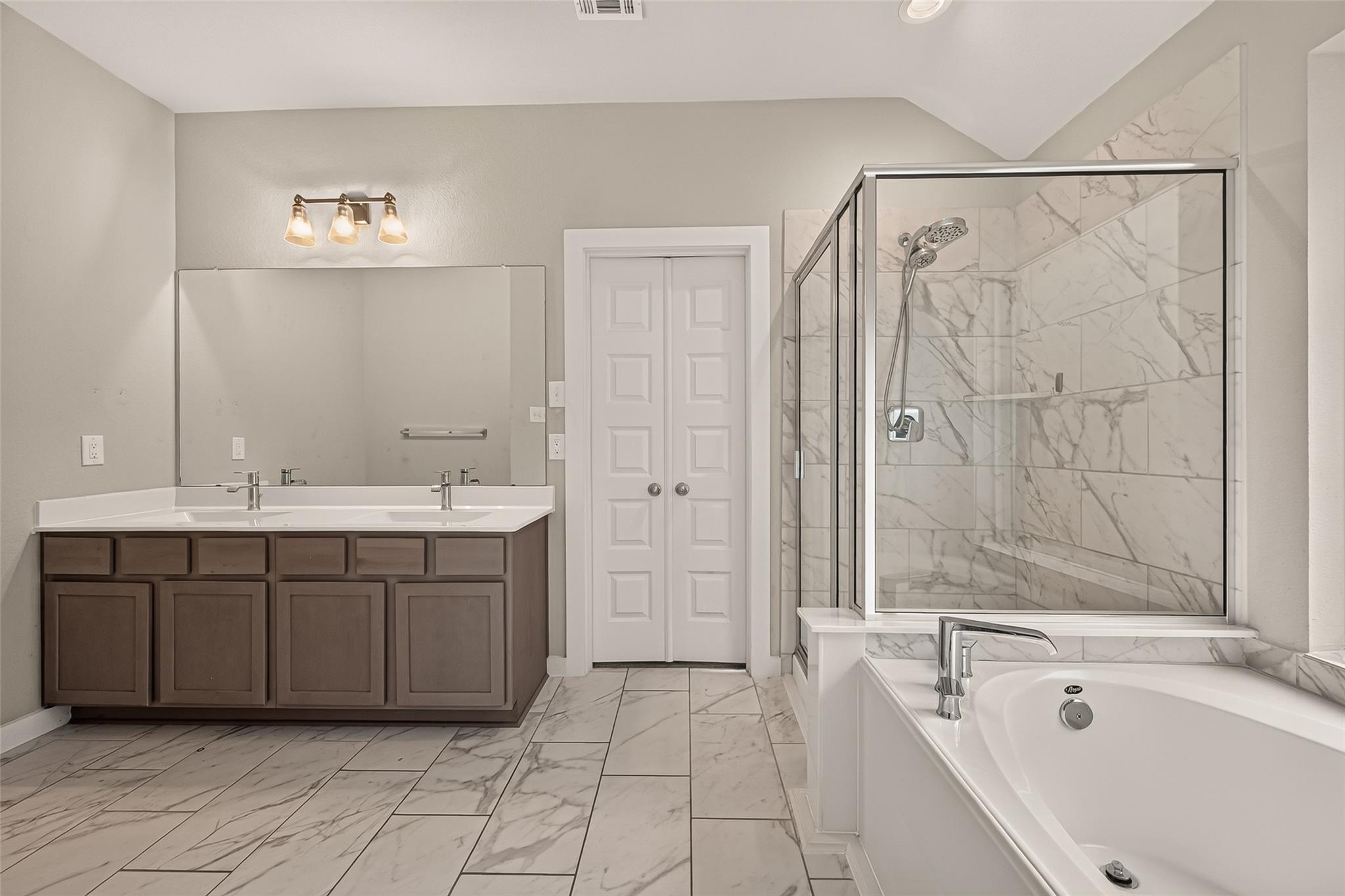 Bathroom with a double vanity, glass-enclosed shower, and soaking tub.