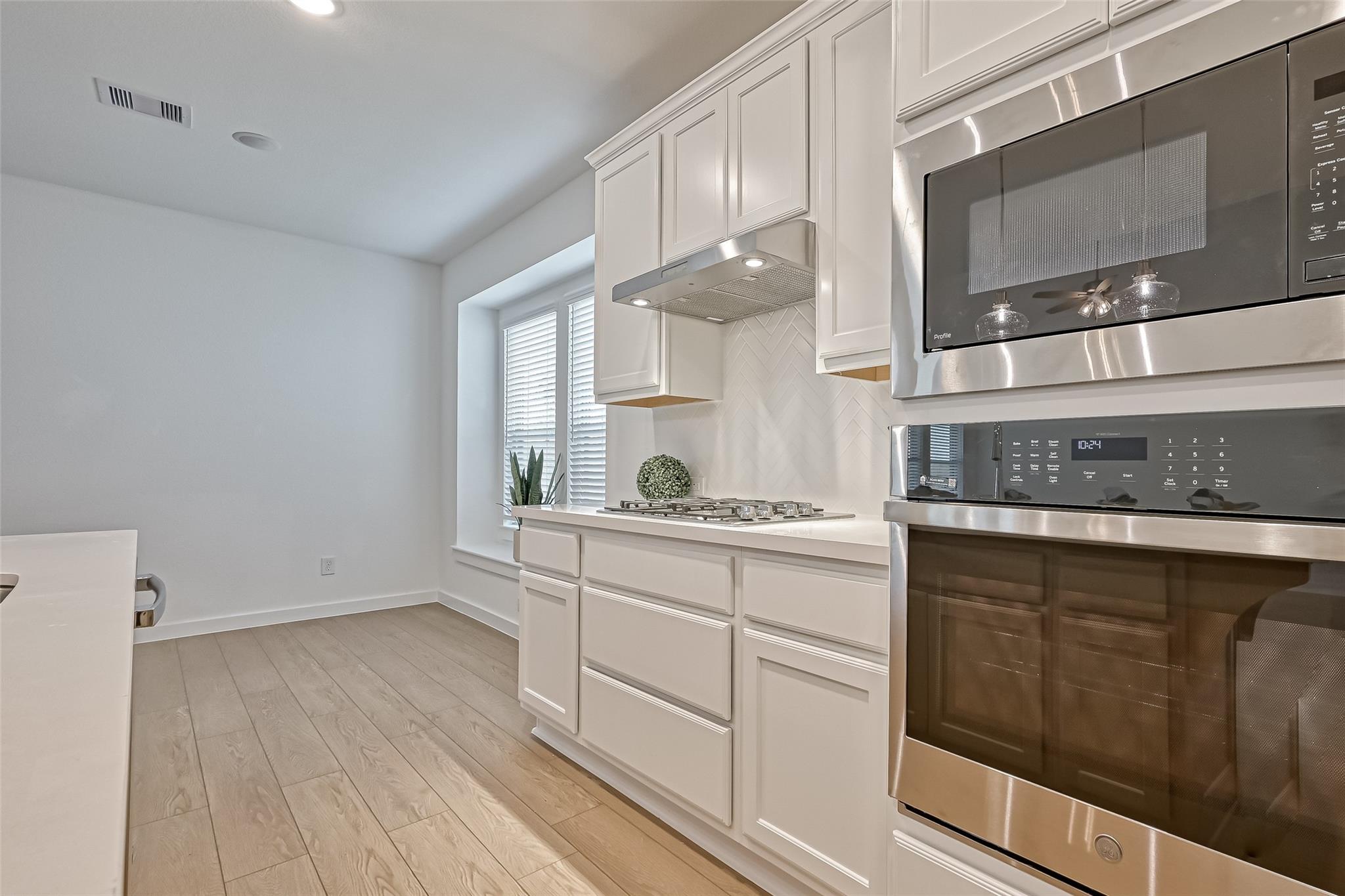 Bright white kitchen with a gas cooktop, herringbone backsplash, and stainless steel double oven.