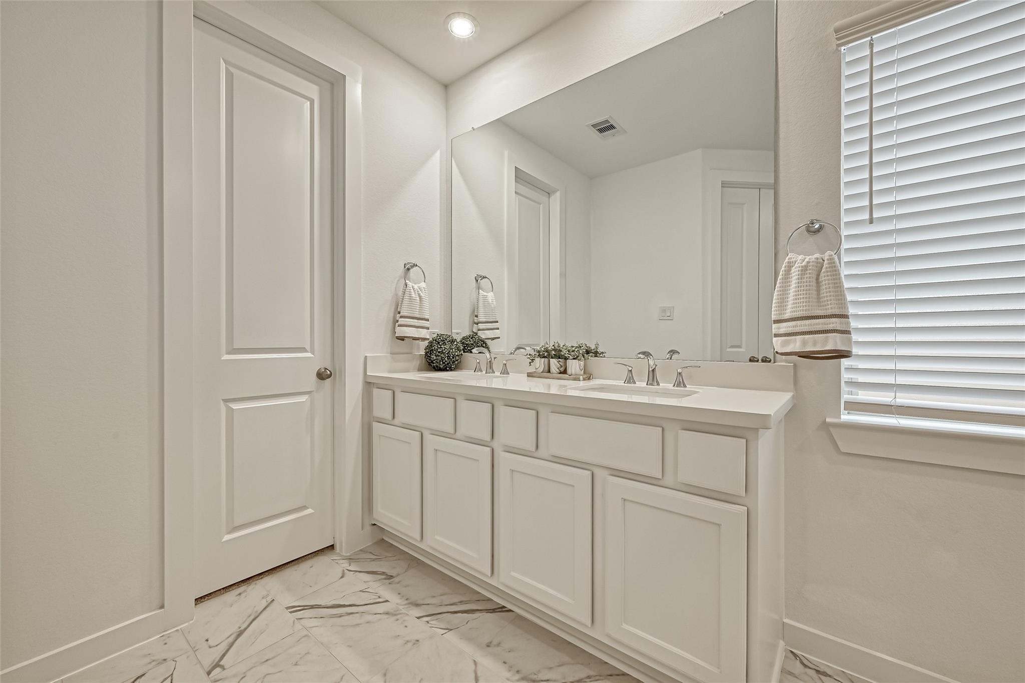 Bright bathroom with a white double vanity, large mirror, and marble-look tile flooring.