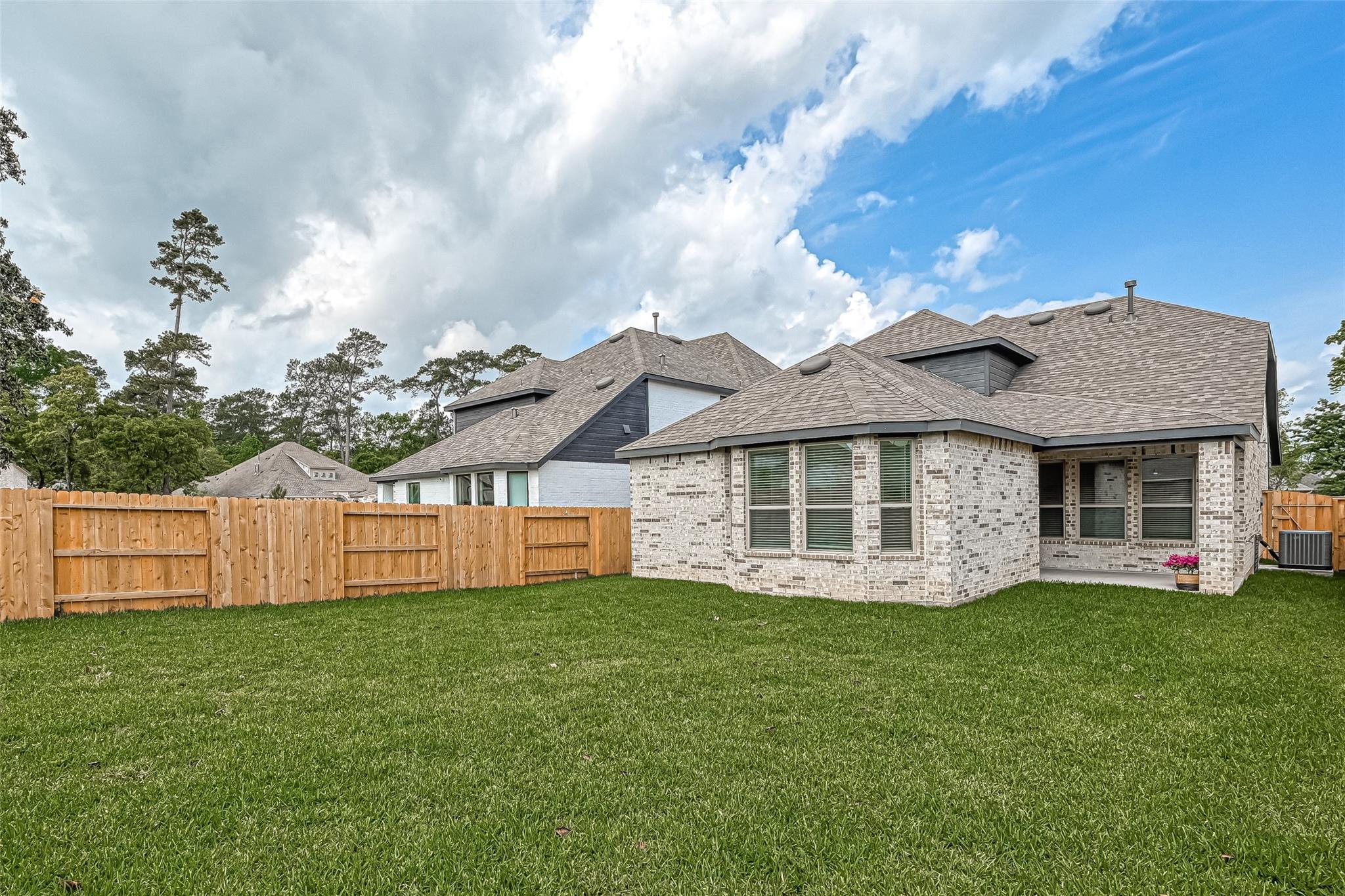 Brick house rear with a covered patio, broad lawn, and wooden privacy fence.